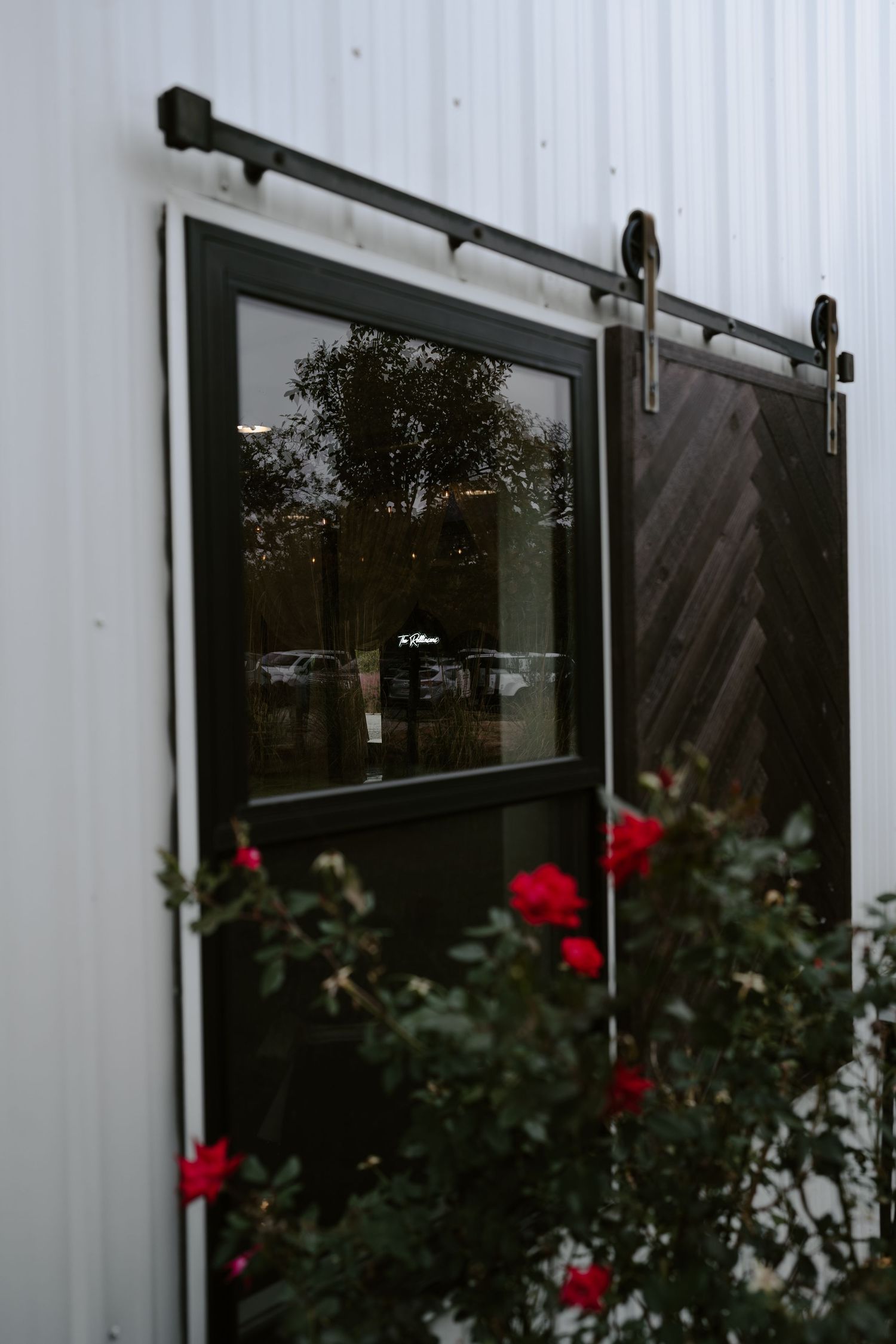 Black sliding barn door with red rose bushes growing alongside white exterior wall.