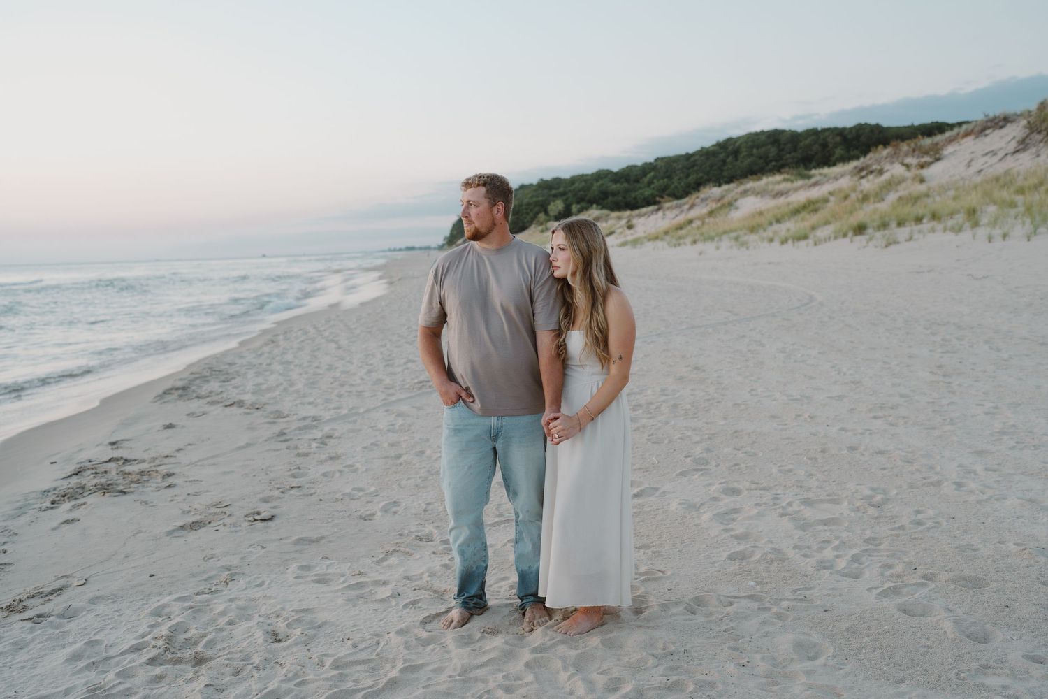 Wide angle shot of couple standing together on beach near sand dunes.