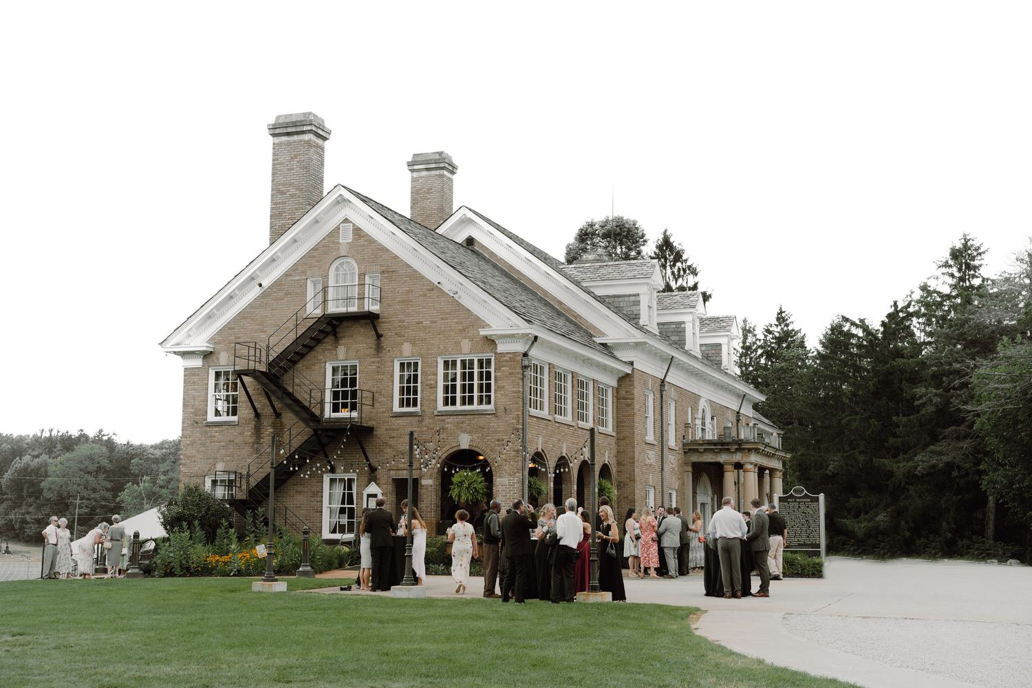 Large elegant stone mansion wedding venue with guests gathered outside on a cloudy day.