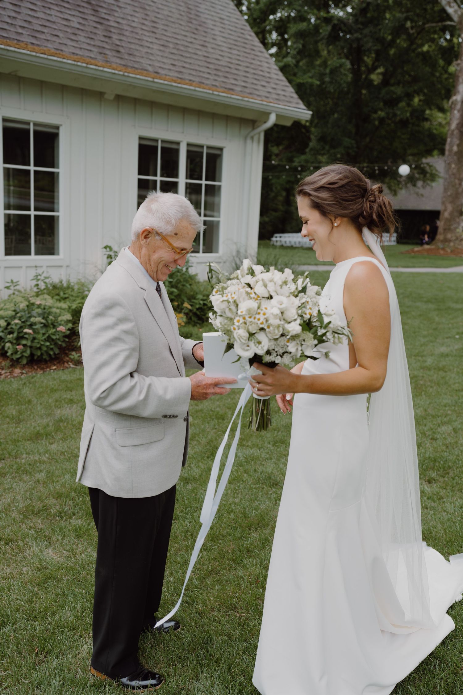 Emotional wedding moment captured with white floral bouquet against white building backdrop.
