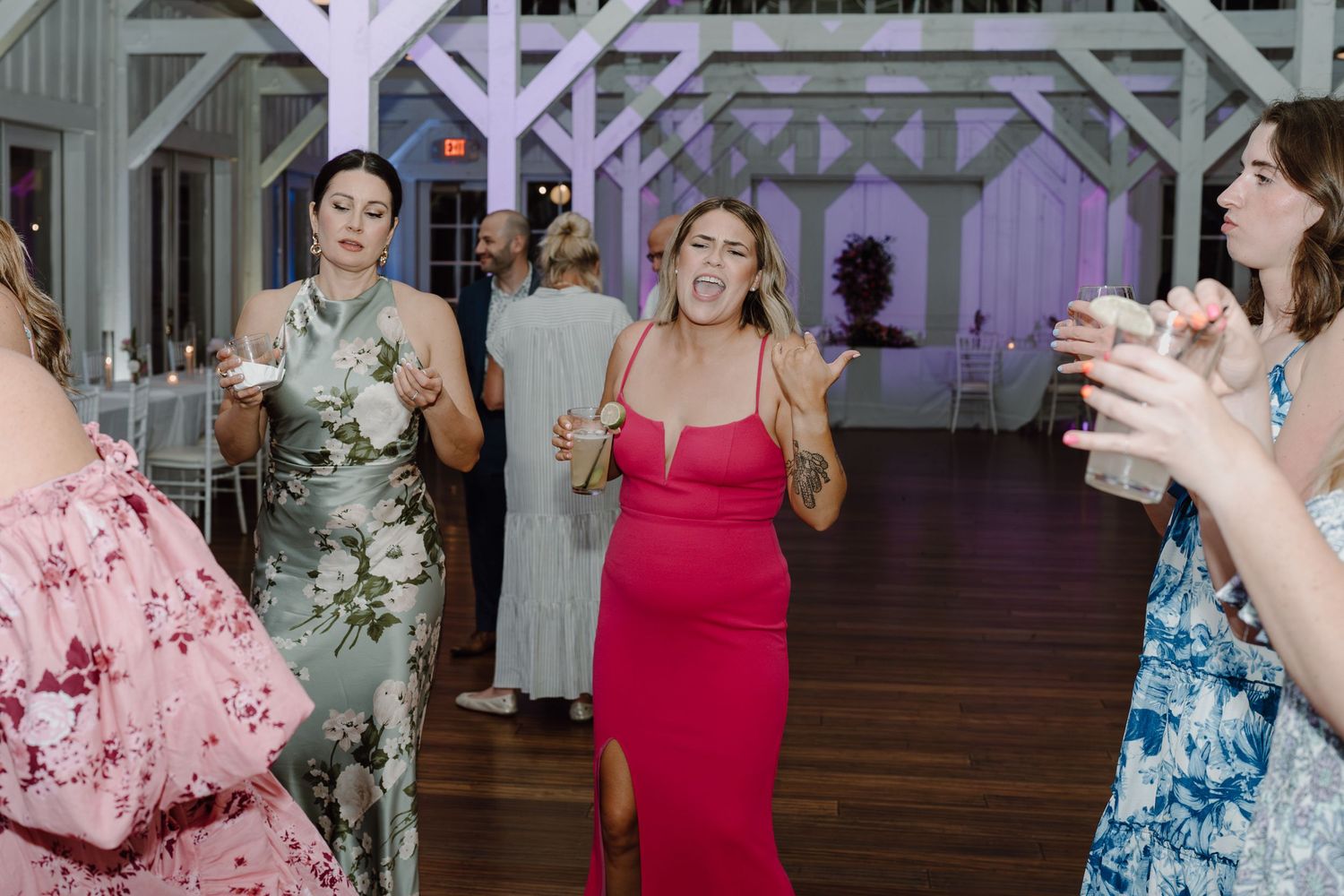 Guests in colorful summer dresses dance and laugh together at an indoor reception.