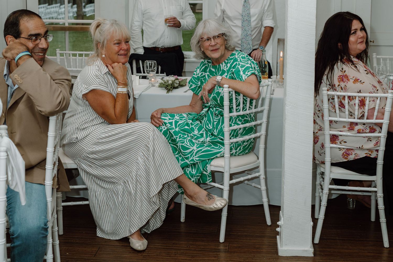 Wedding guests seated at white tables in an elegant white barn venue during a reception celebration.