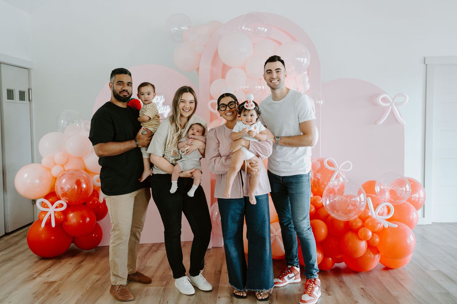 Celebratory scene with festive balloon arch in coral and pink tones against white backdrop.