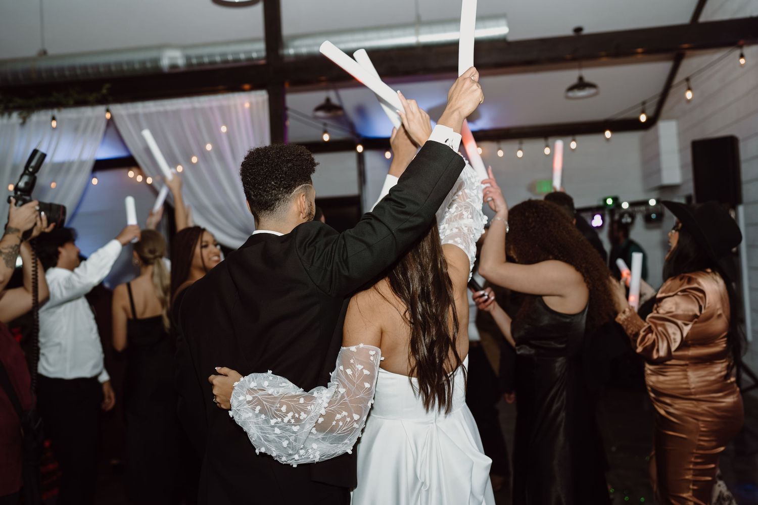 Wedding guests dance with glowing foam sticks during a lively reception celebration.