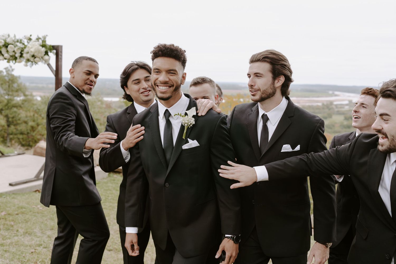 Groomsmen share an entertaining moment during outdoor wedding photography session.