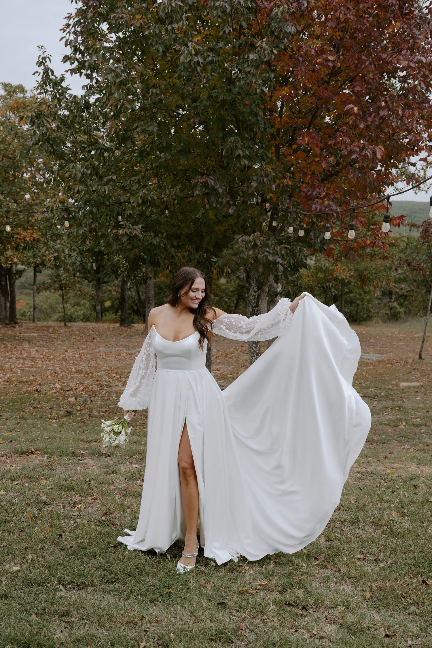 Flowing white wedding dresses photographed against autumn trees and fallen leaves.