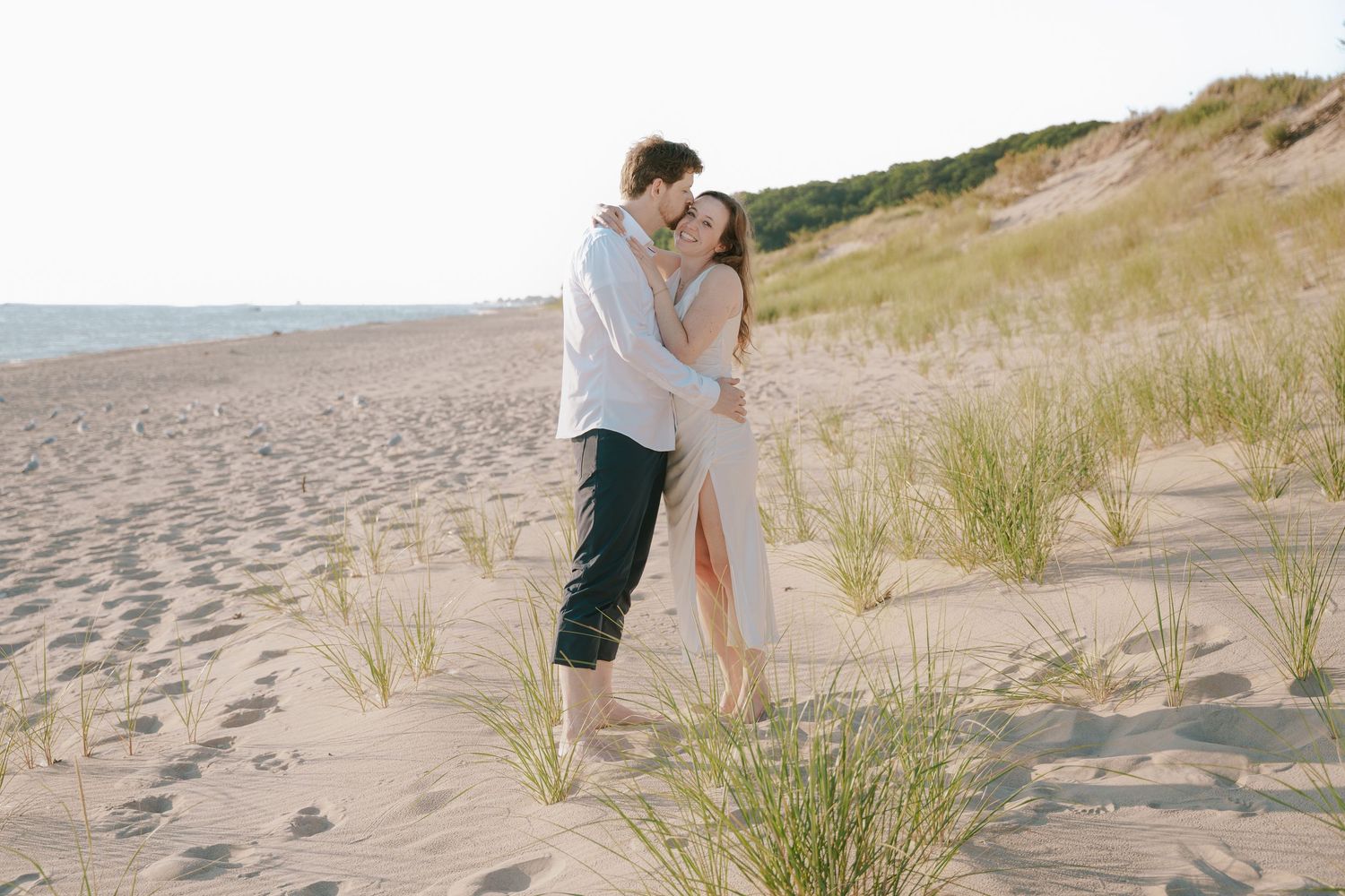 A couple shares a romantic moment among beach grass and sand dunes.