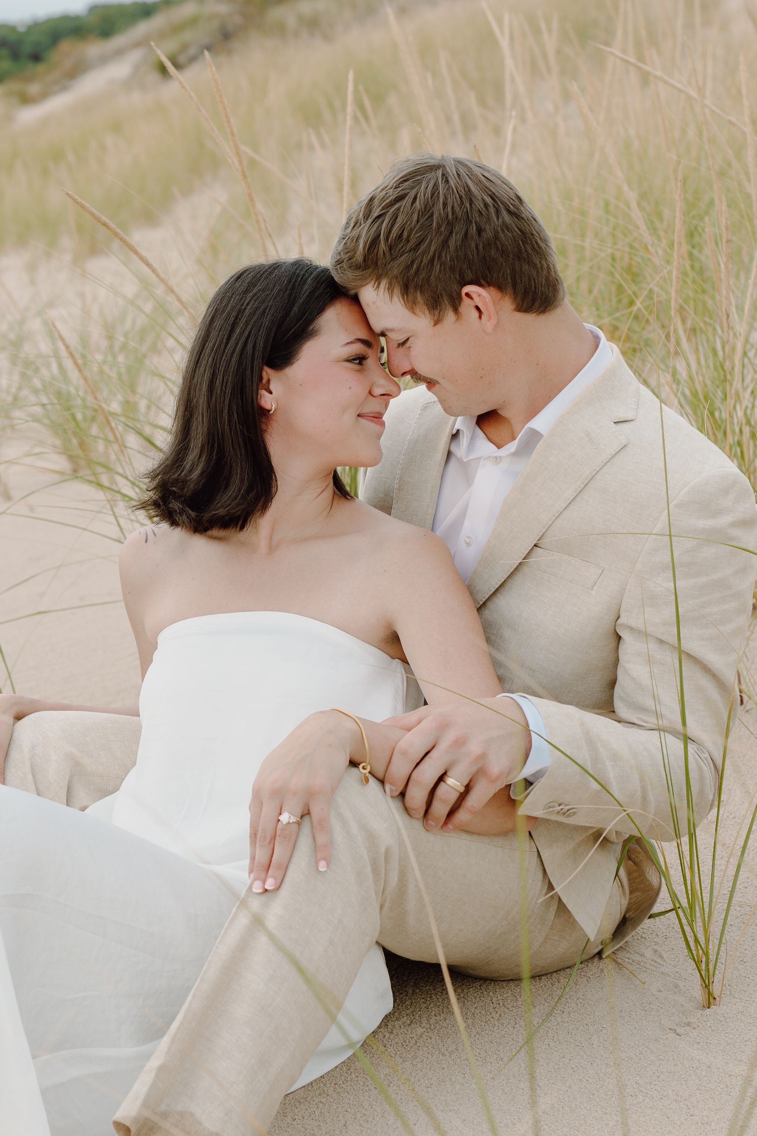 Intimate beach portrait of couple in white embracing among dune grass.