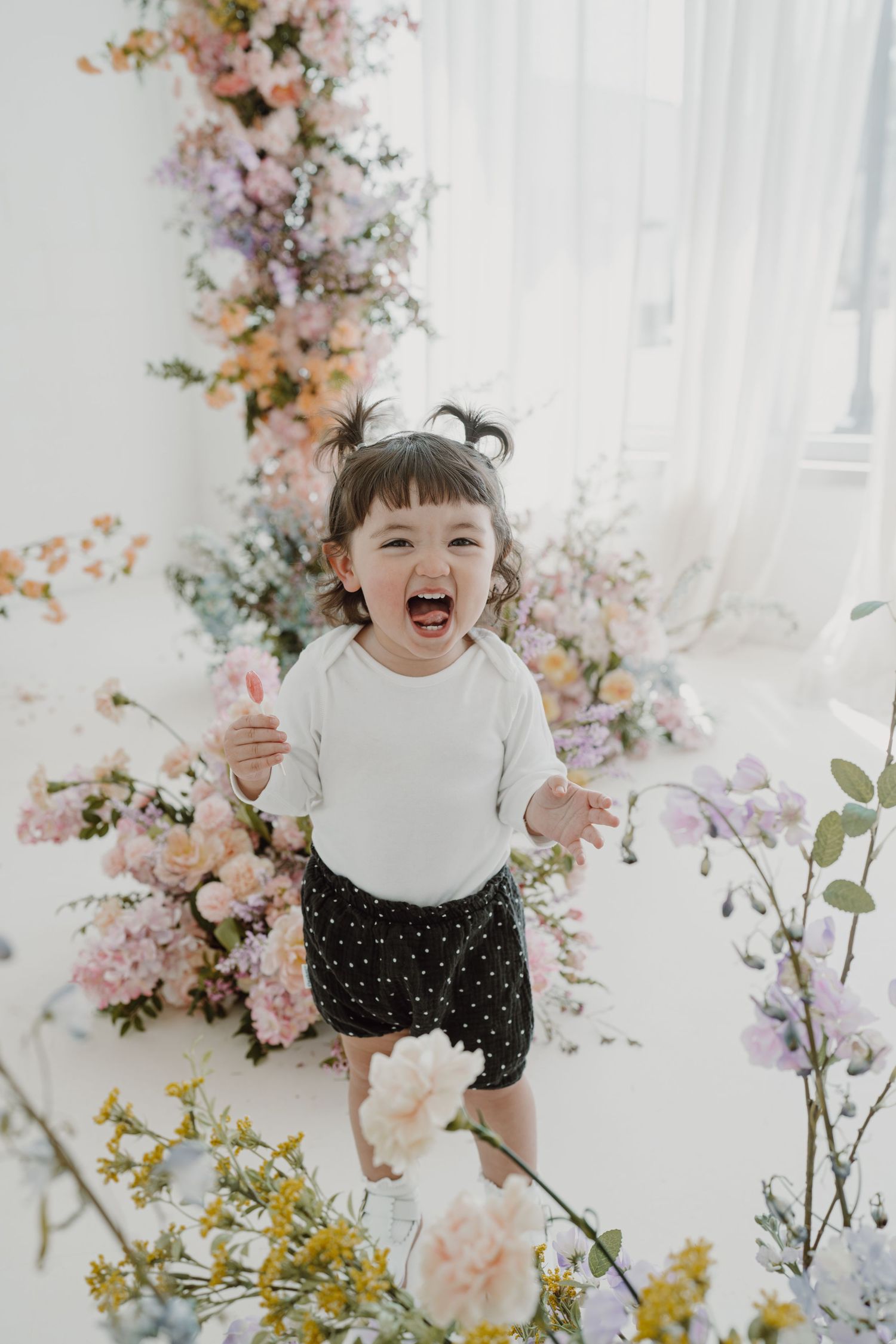 Joyful child playing among pink and yellow floral arrangements in a bright studio.