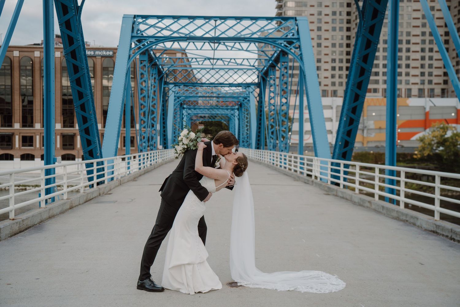 Elegant wedding couple sharing intimate moments on an urban blue bridge walkway.