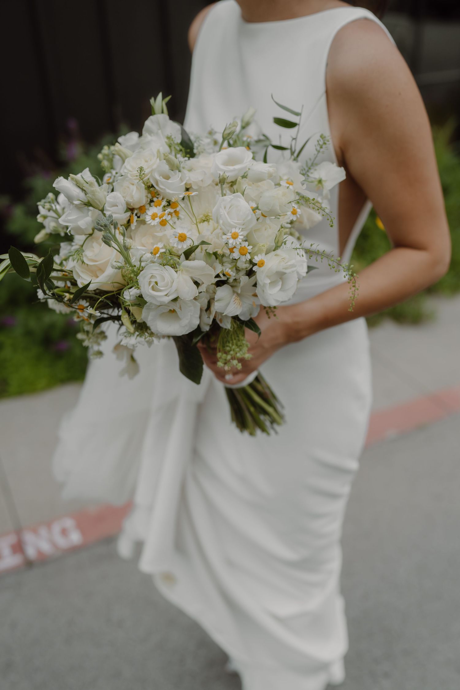 Elegant white bridal bouquet with roses and daisies against white wedding dress.