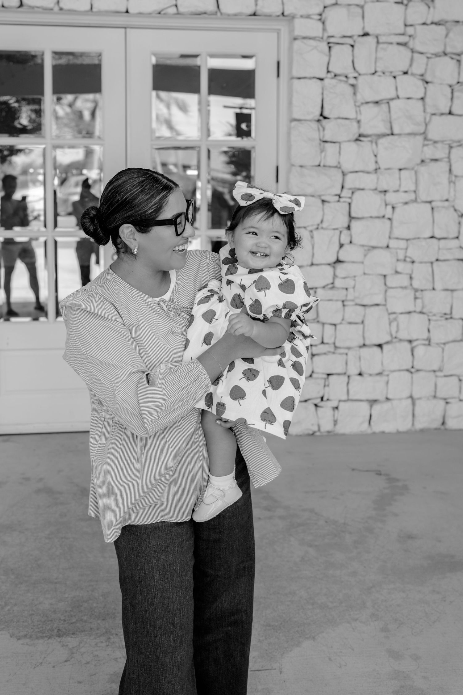 Black and white photo of parent and child in playful pose against stone wall.