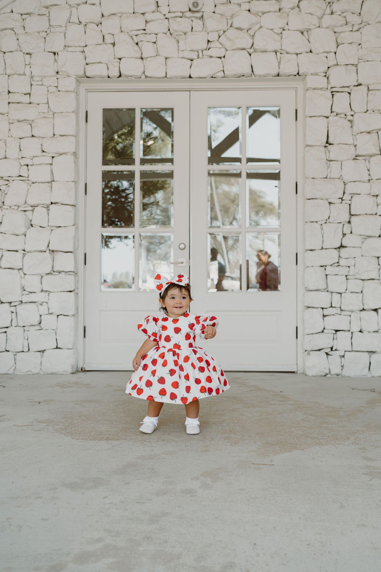 Sweet heart-patterned dress and matching bow accessory against a white stone wall backdrop.