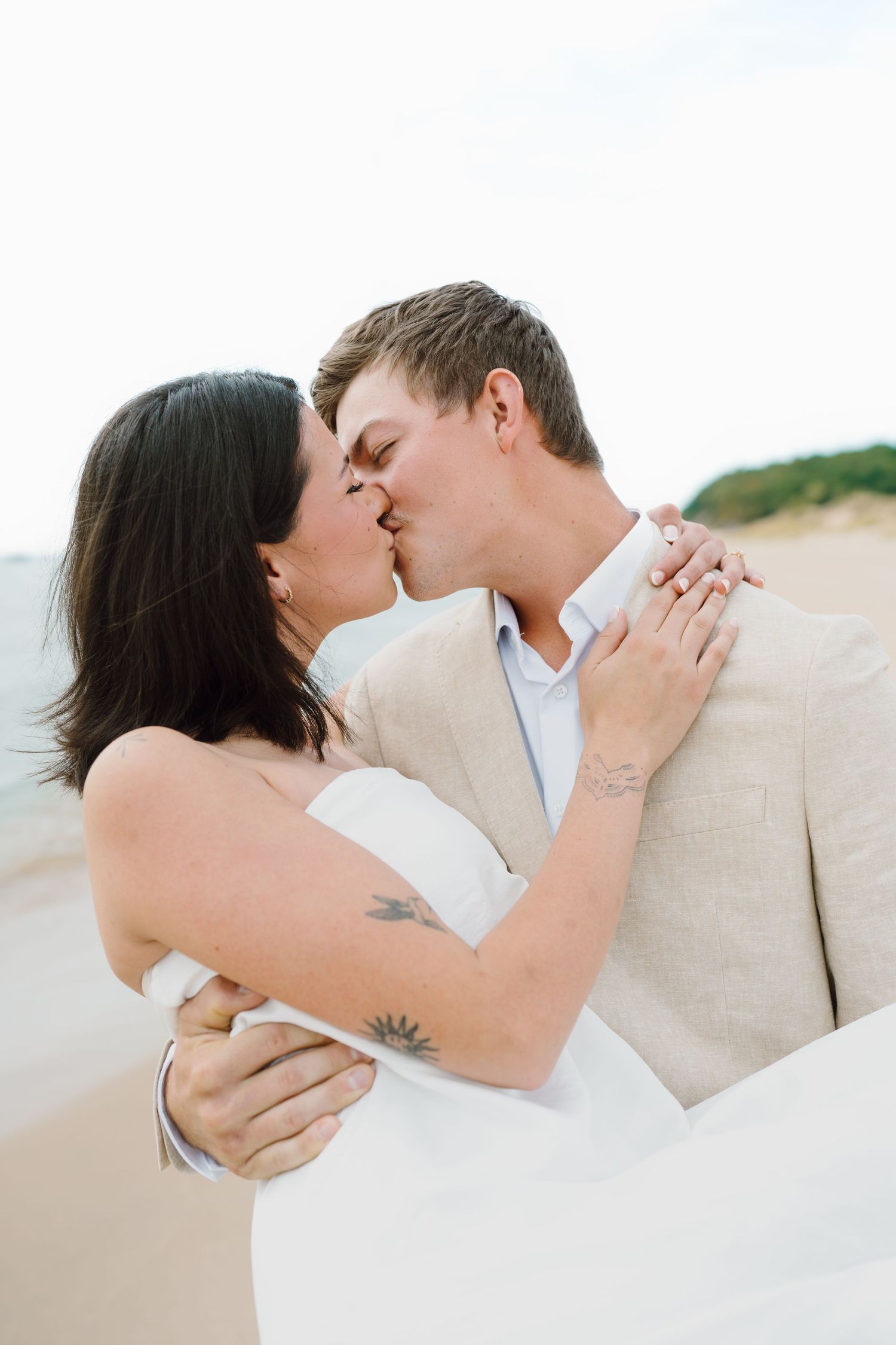 Soft focus beach portrait of couple in white and beige sharing romantic moment.