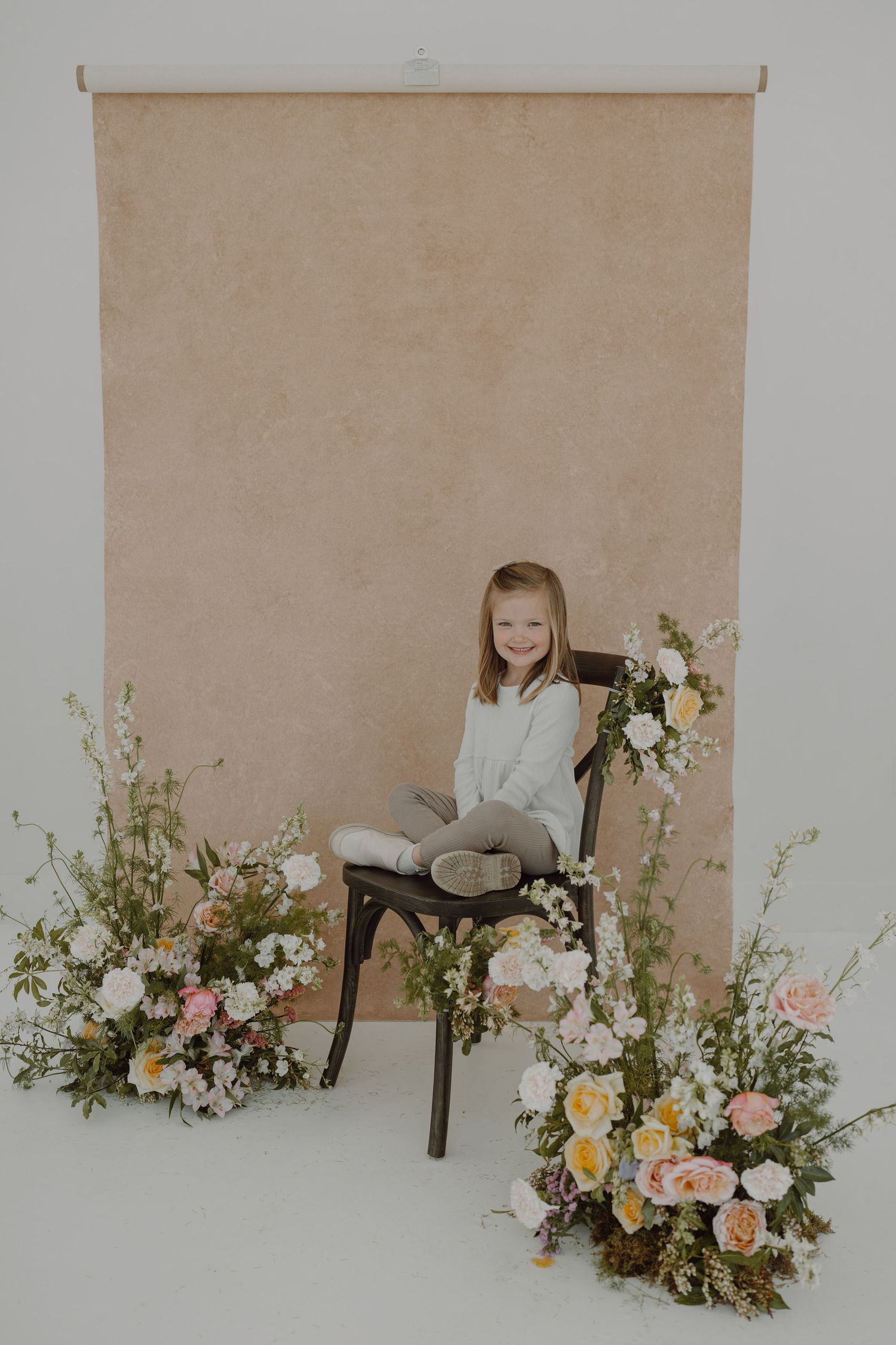 Studio portrait setup with elegant floral arrangements and a wooden chair against a neutral backdrop.