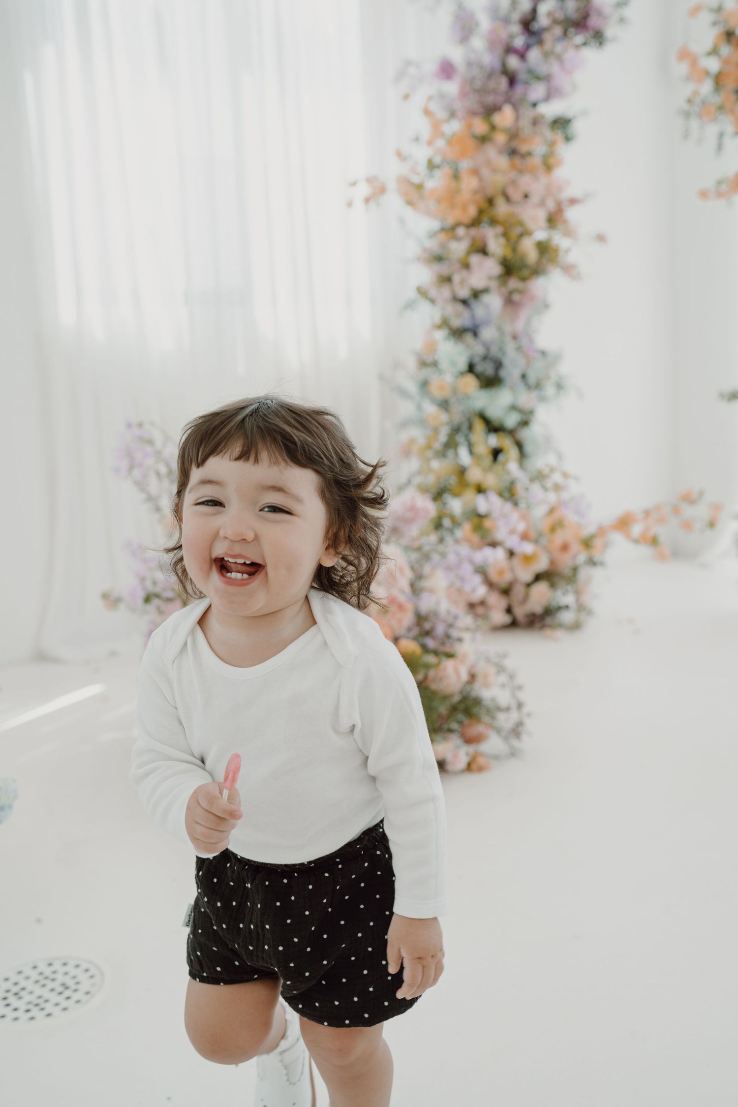 Happy toddler laughing and playing in white studio with floral decorations.