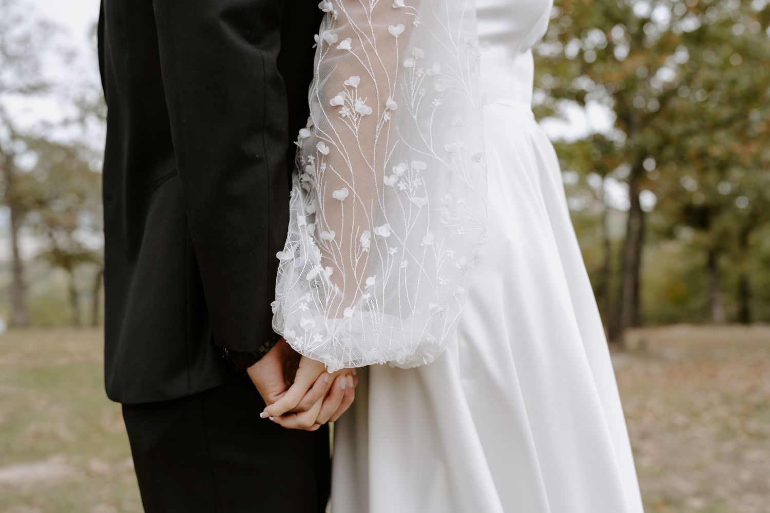Close-up detail of a bride's lace wedding dress sleeve against a black suit.