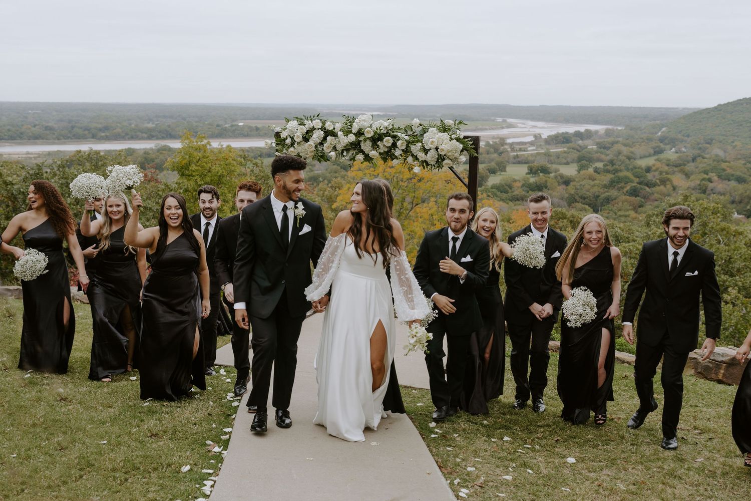 Wedding party and guests assembled along white pathway during outdoor hilltop celebration.