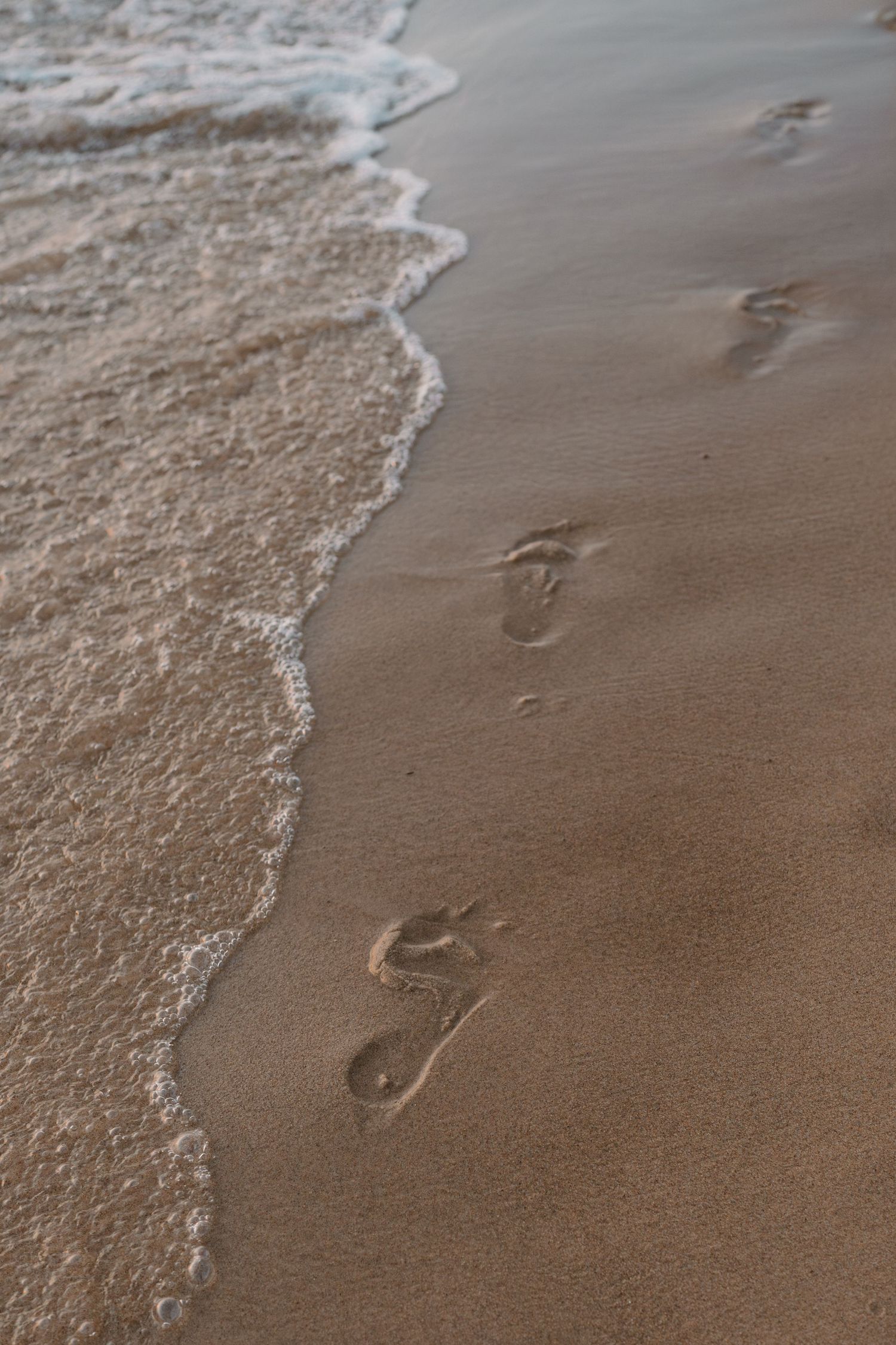 Close-up of gentle waves washing over footprints in wet sand.
