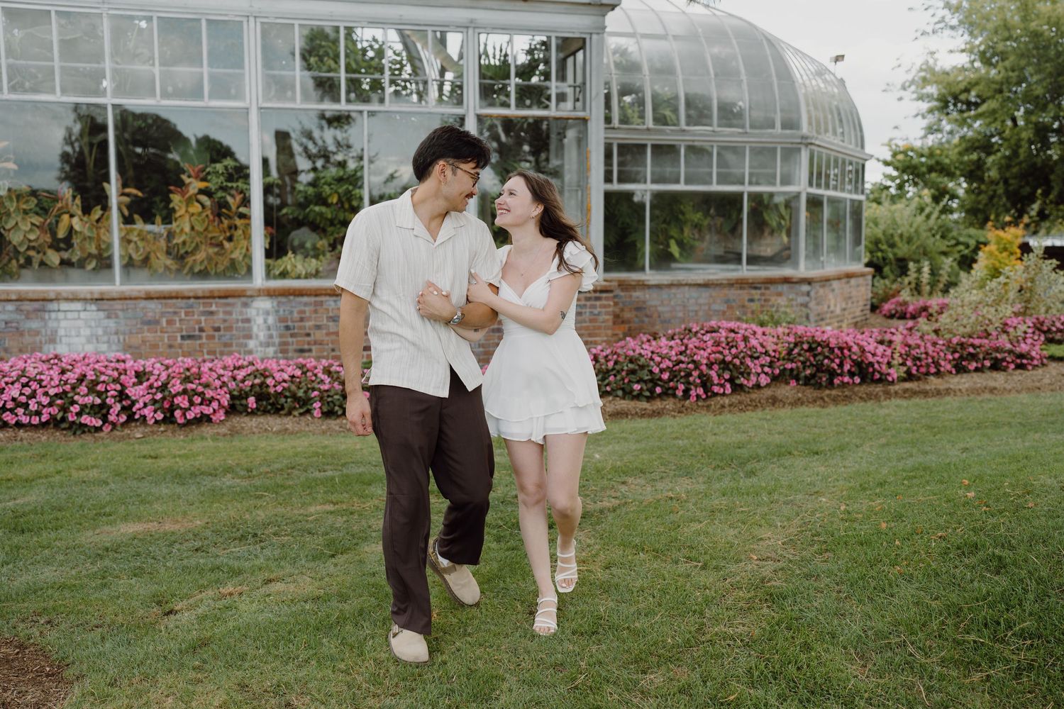 A couple shares intimate moments during their outdoor photoshoot near a greenhouse.