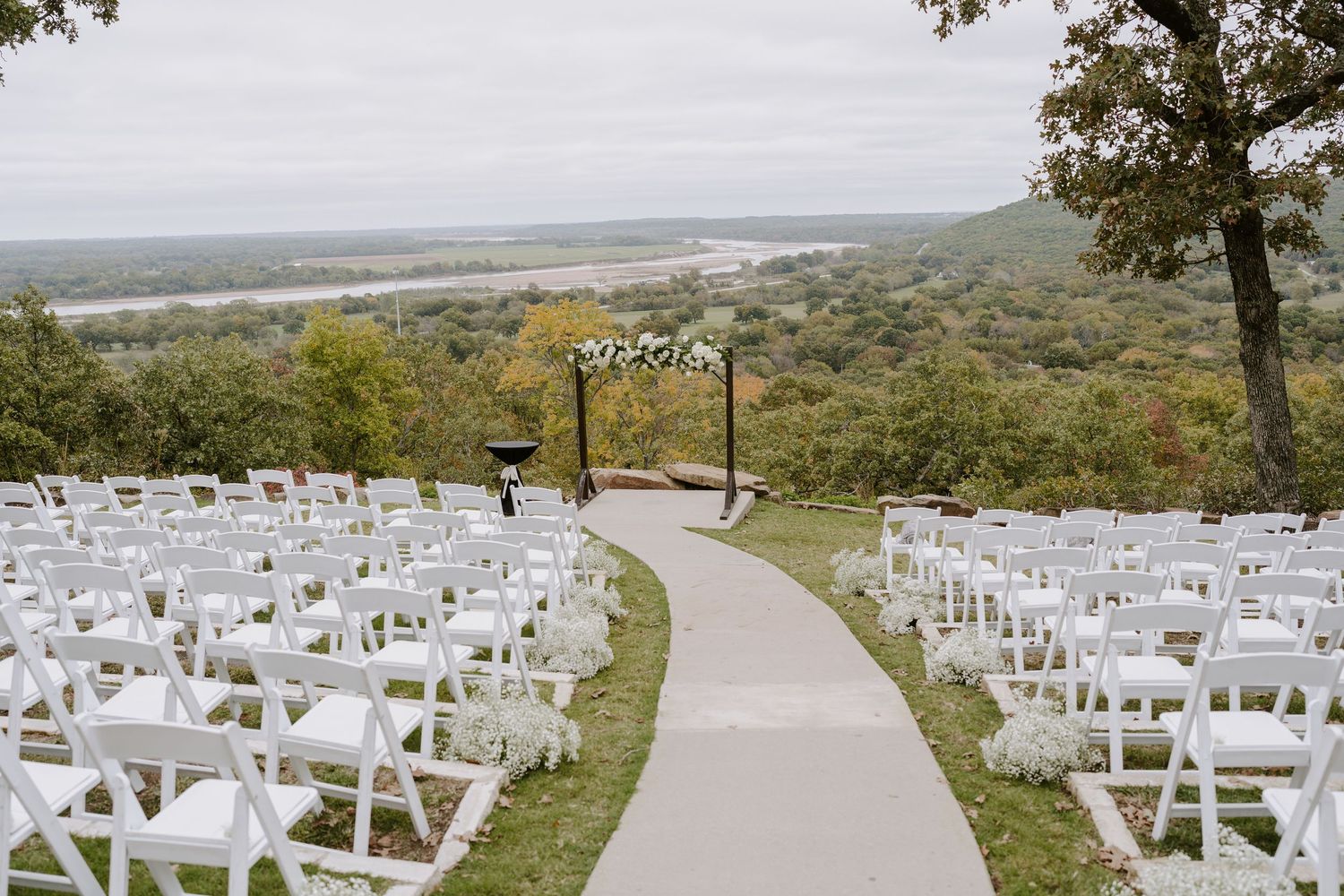 Outdoor wedding ceremony setup with white chairs arranged on a hillside overlooking scenic views.