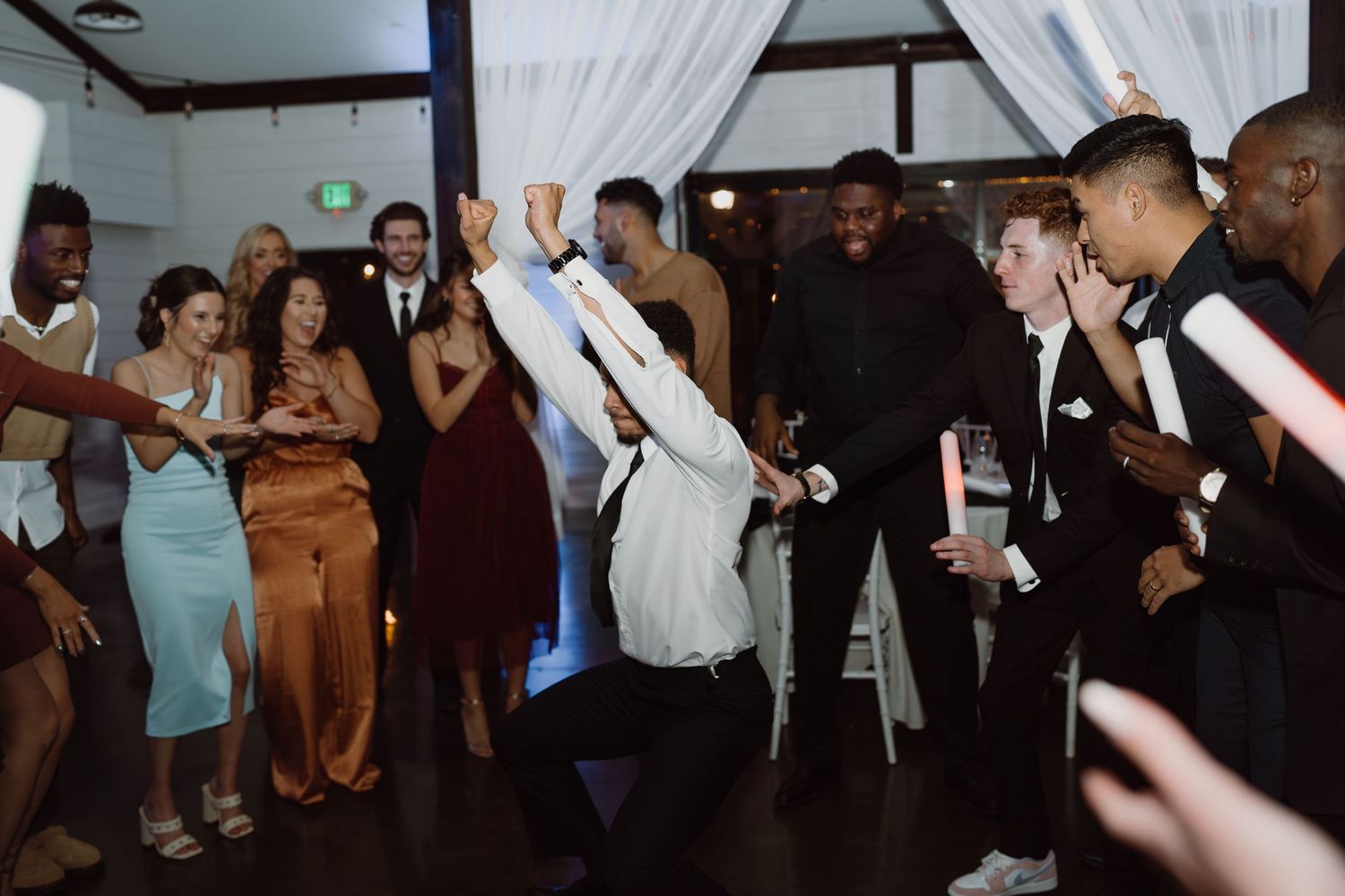 Wedding guests dance and celebrate on a dimly lit dance floor during an energetic reception party.