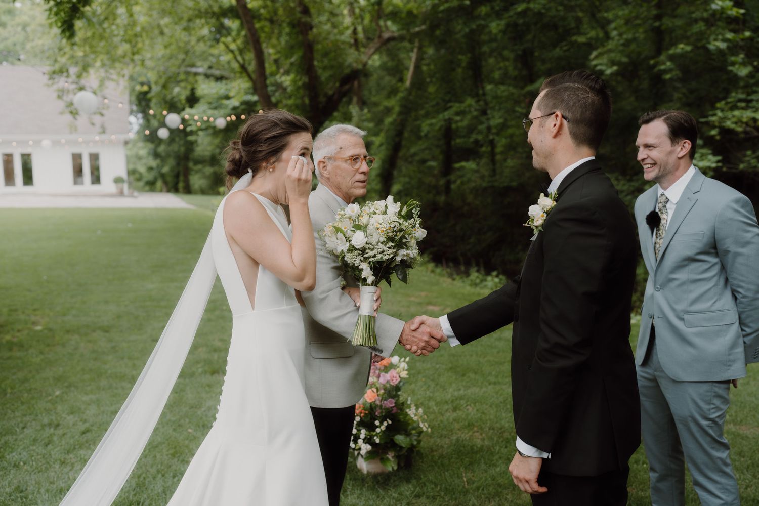 Outdoor wedding ceremony in progress with guests and floral arrangements in a garden setting.