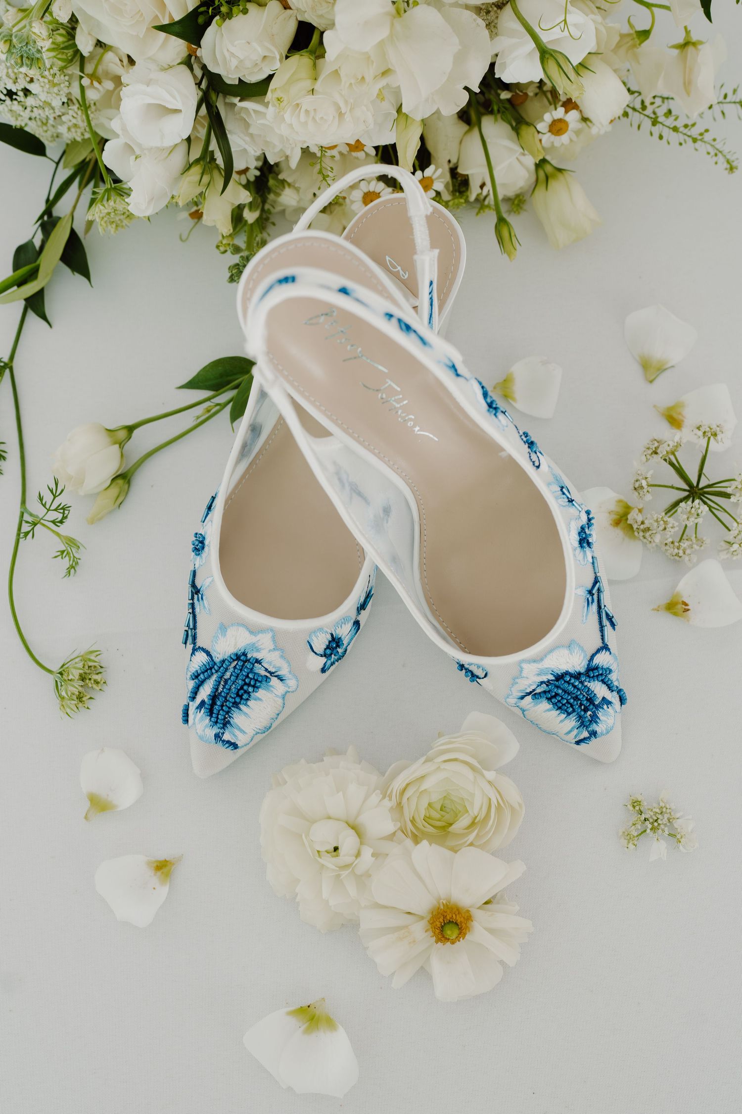 Elegant bridal shoes with blue watercolor pattern surrounded by white floral arrangements.