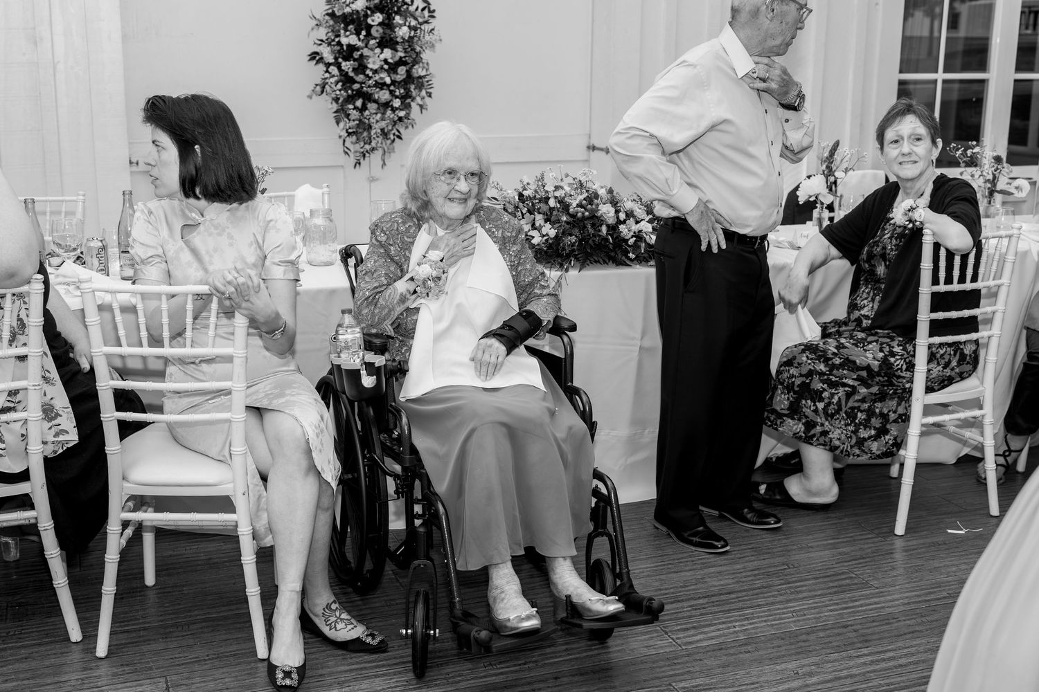 Wedding guests seated in white chairs along the wall during reception celebrations.