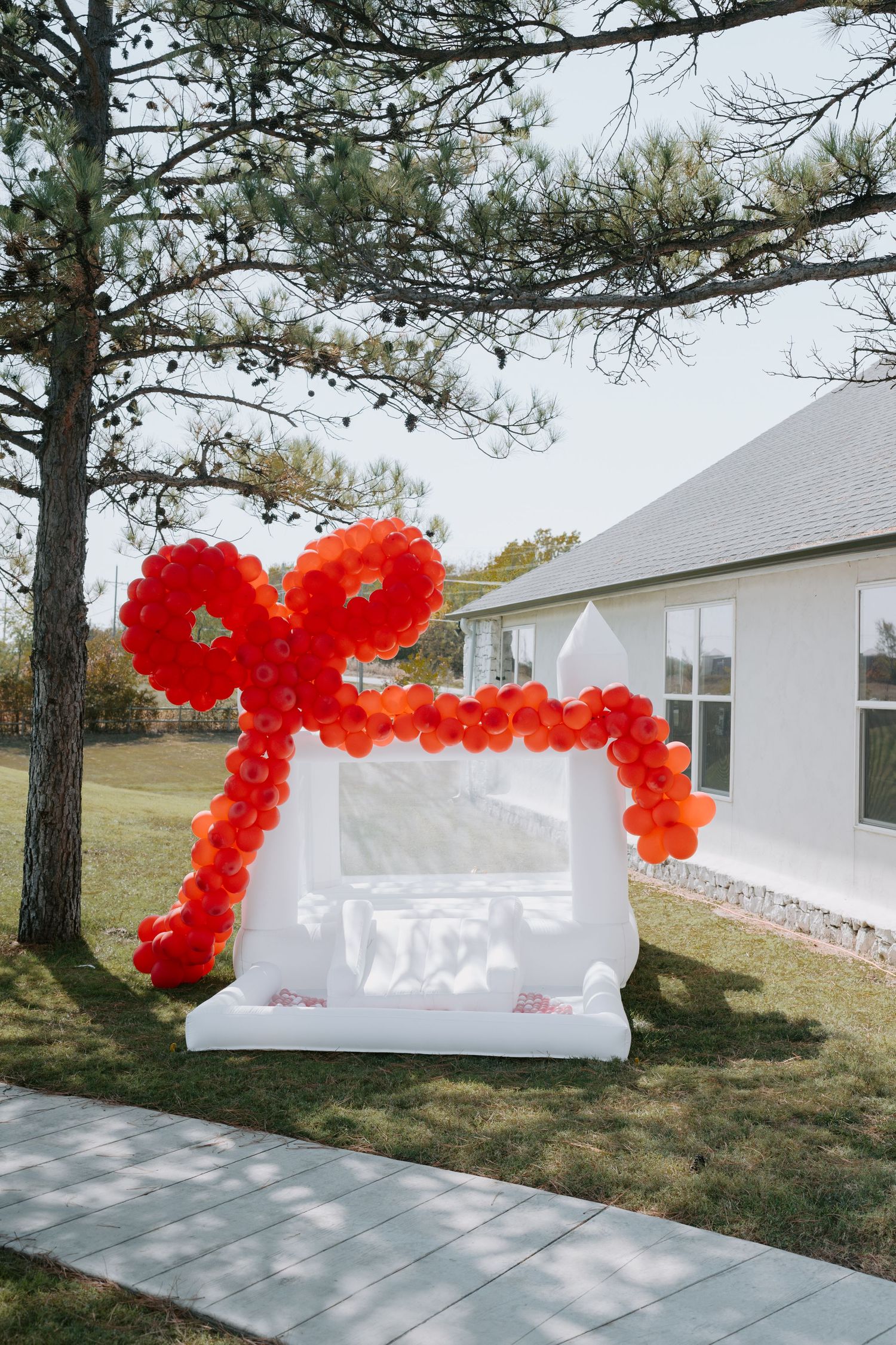 Outdoor view of a white building with red balloon decorations and pine trees.