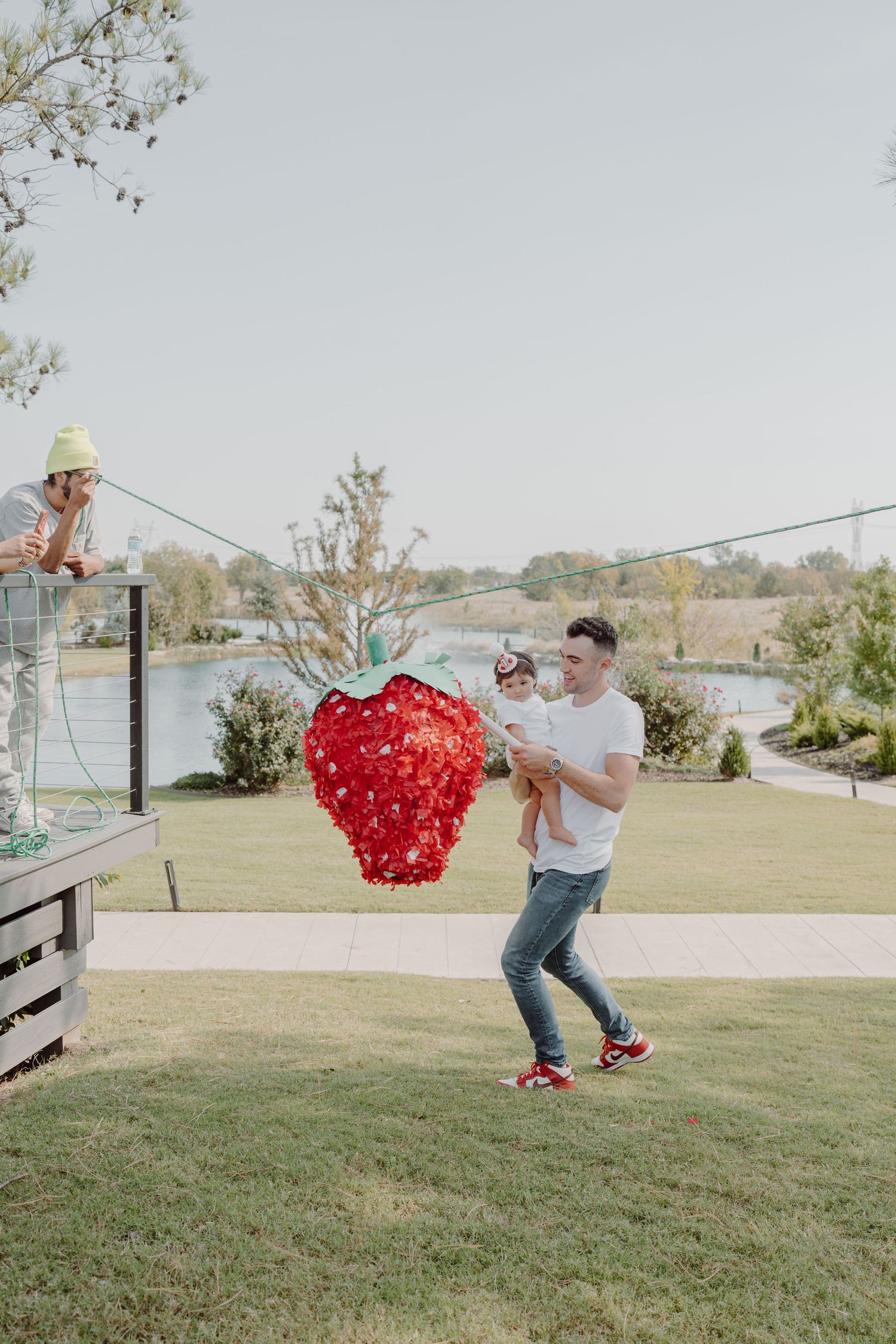 A large red heart-shaped decoration is swung on a string across a grassy lawn on a sunny day.
