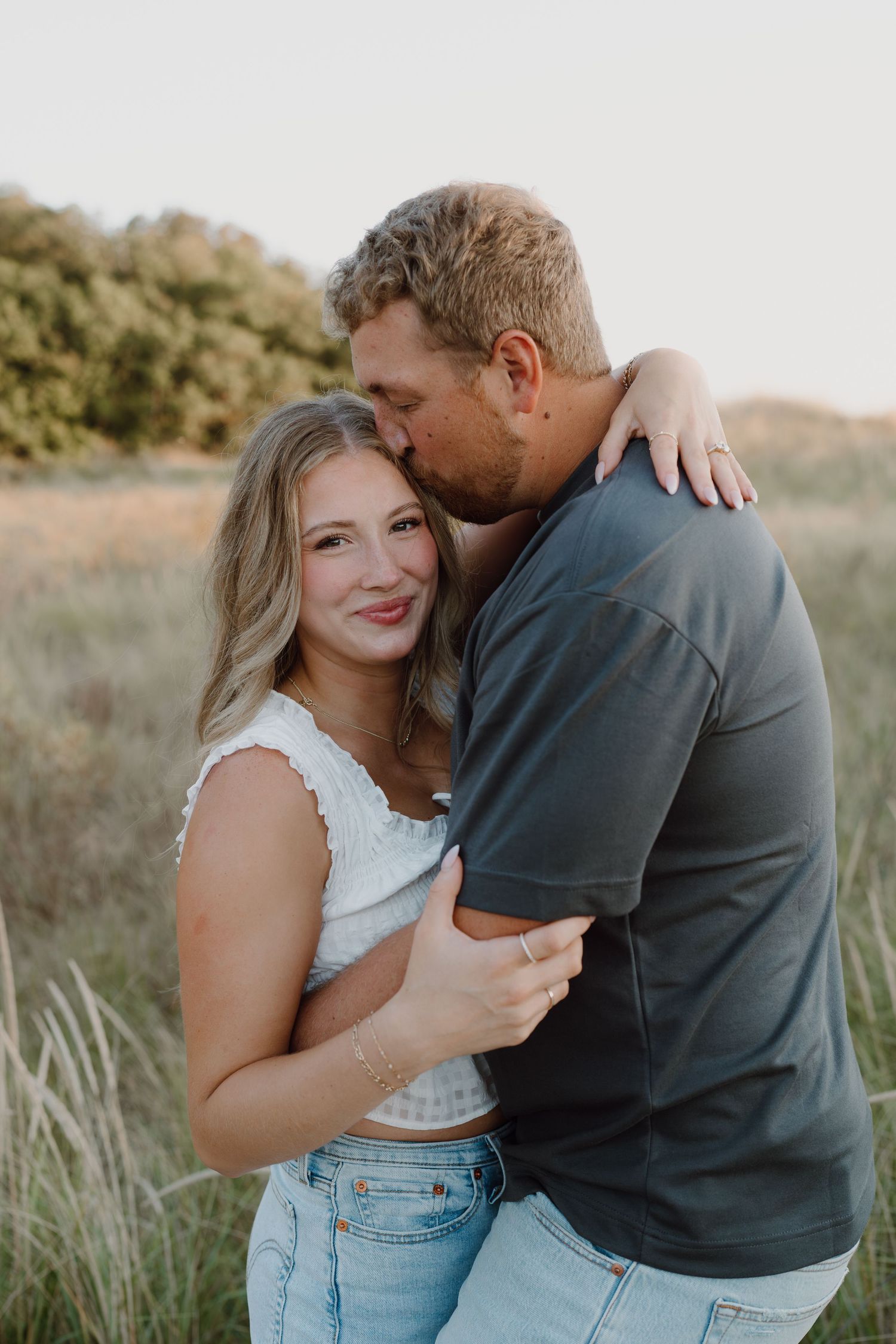 Candid moments between couple during sunset photoshoot on beach dunes.