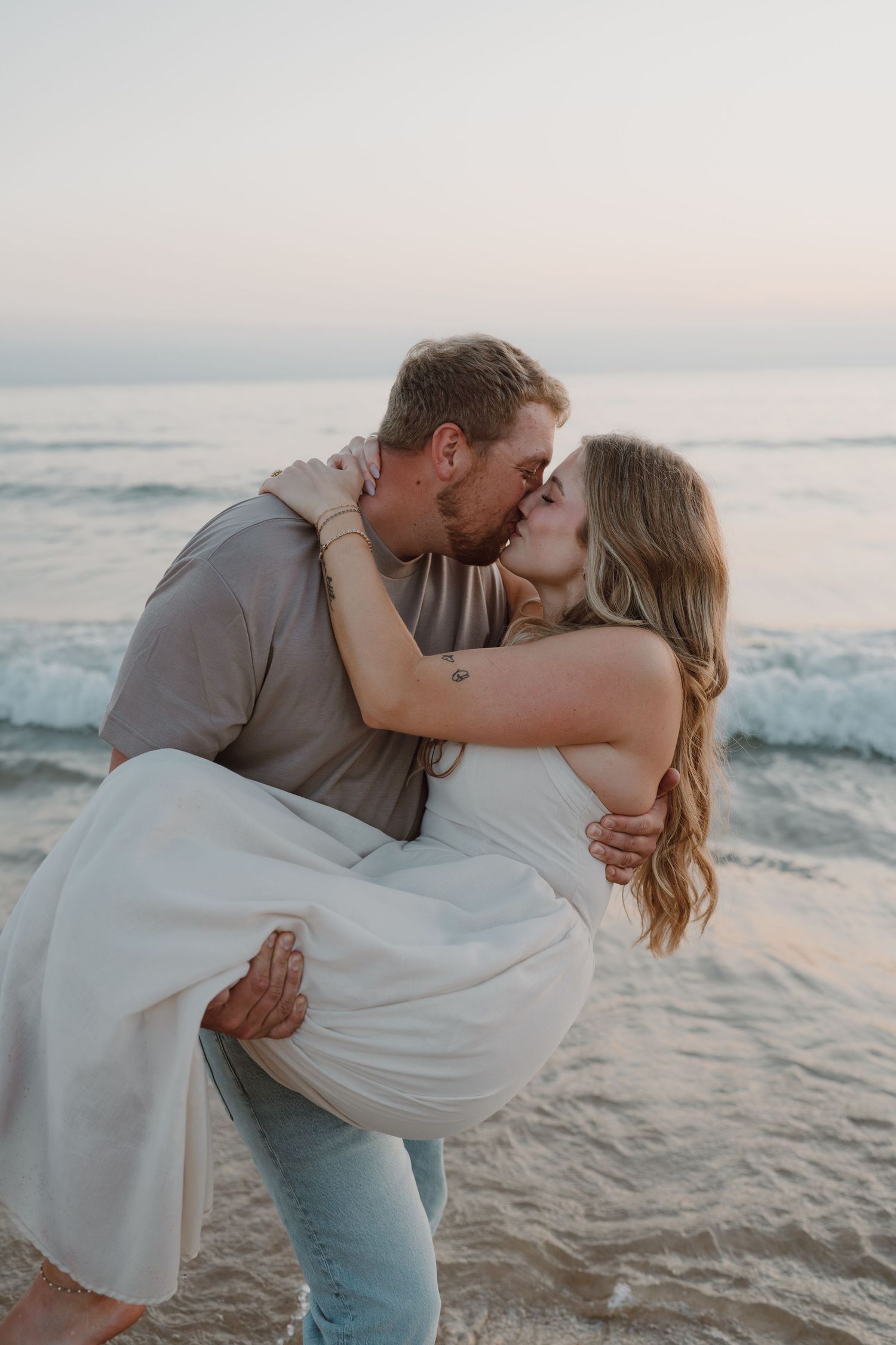 A romantic beachside moment captured during golden hour with waves crashing in the background.