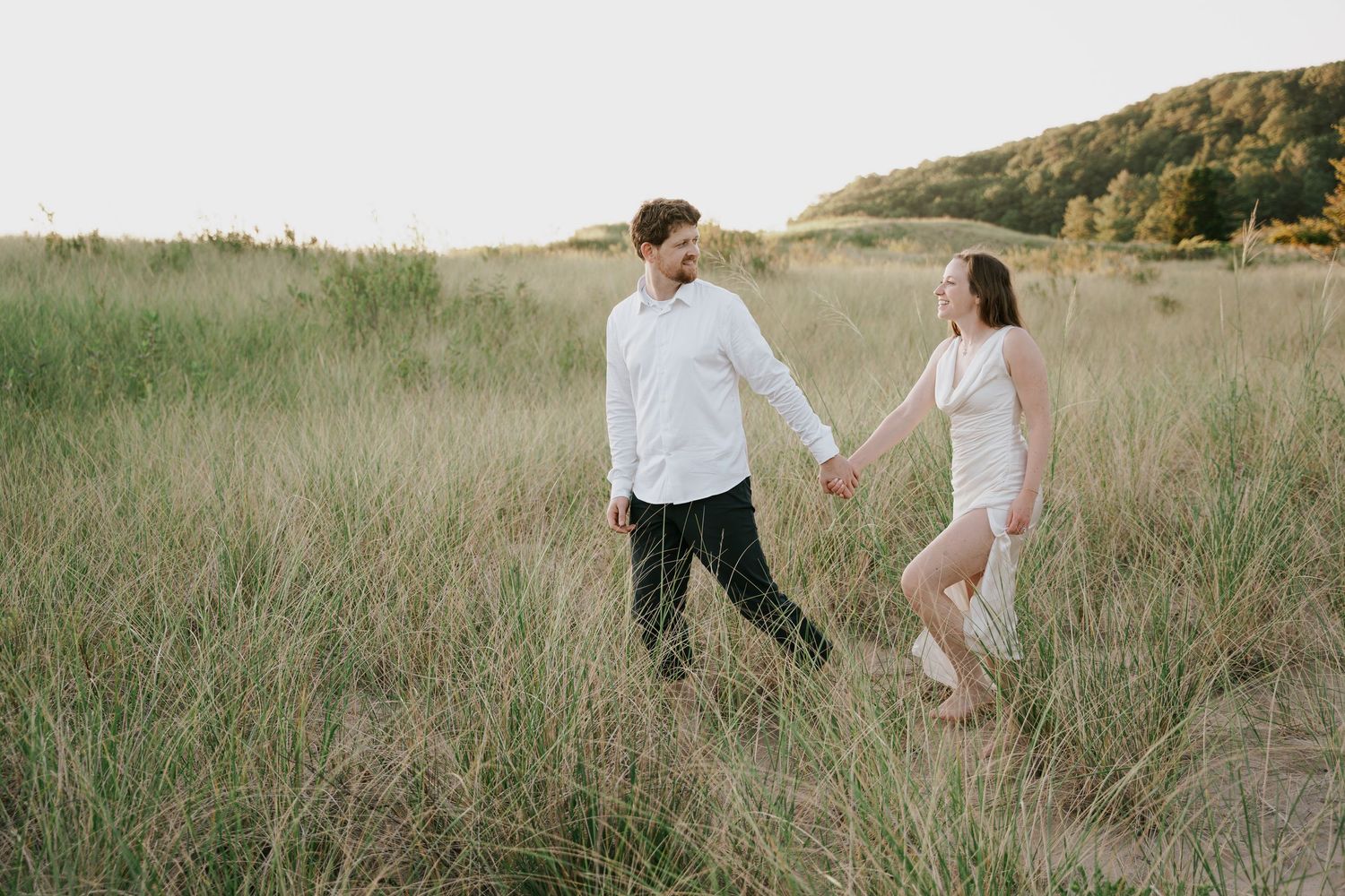A couple explores a scenic hillside meadow together during sunset.