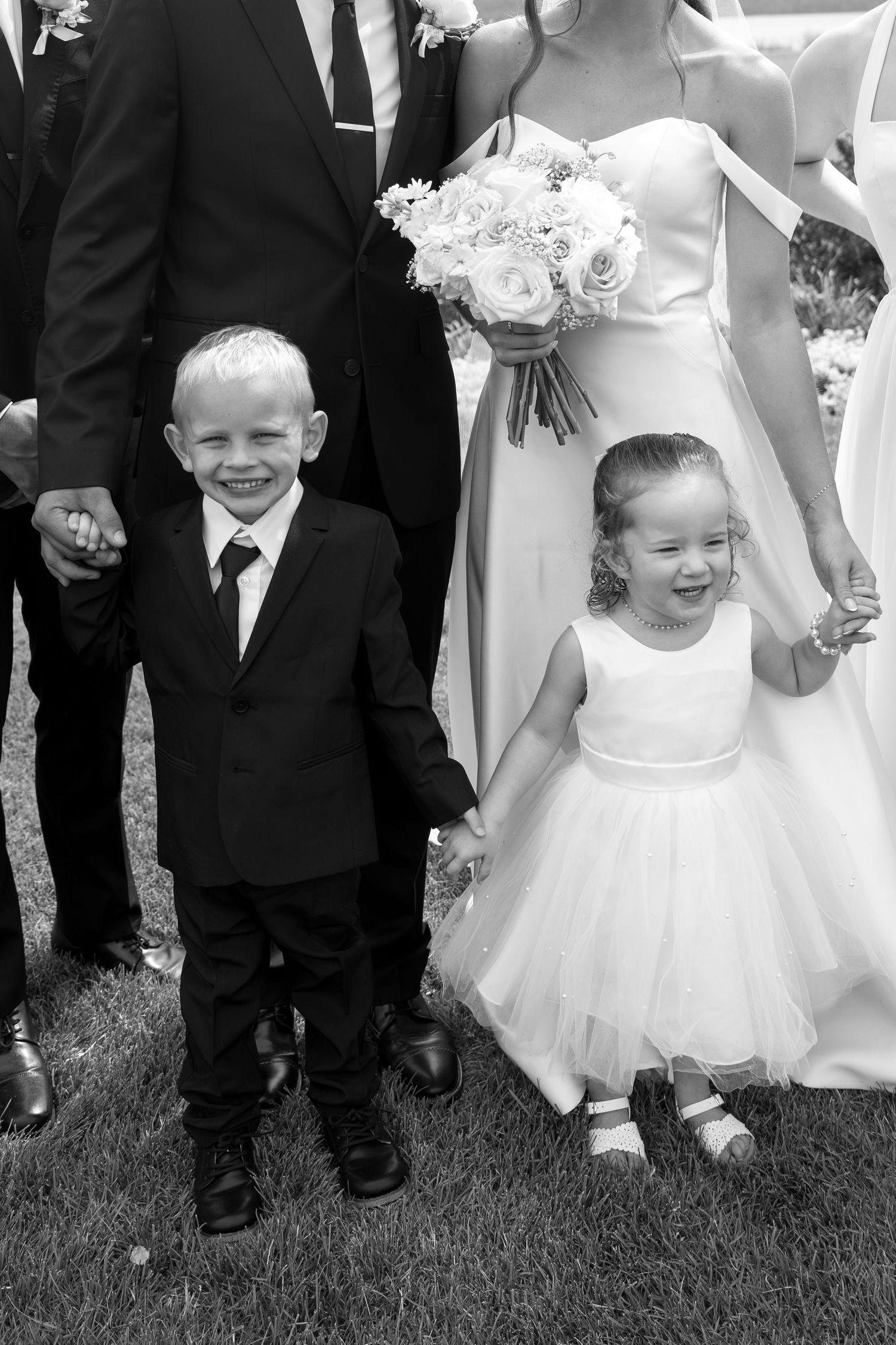 Black and white photo of a young ring bearer in a suit and flower girl in white dress smiling at a wedding.