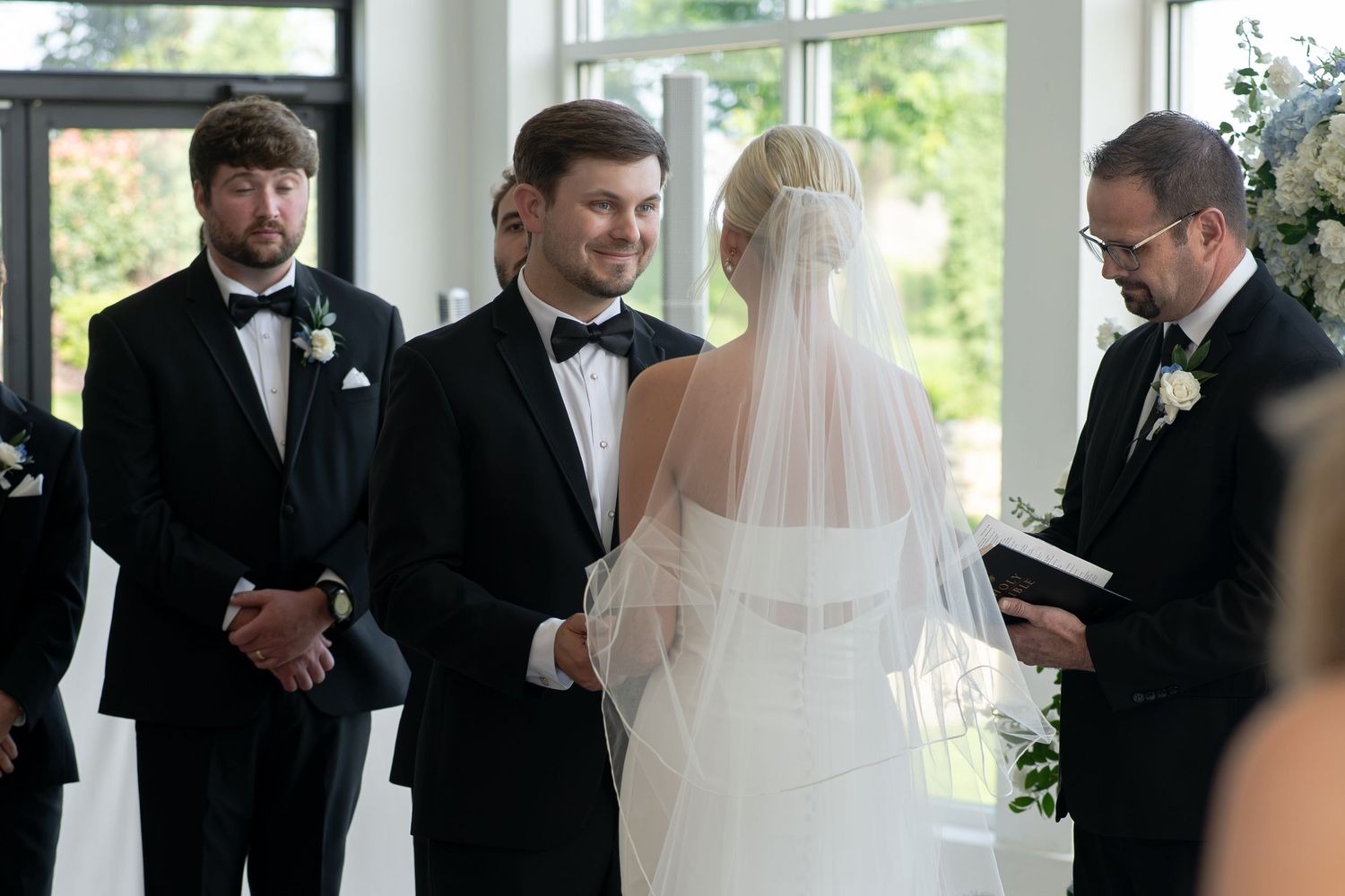 Bride and groom exchange vows at elegant indoor wedding ceremony with officiant and groomsmen.