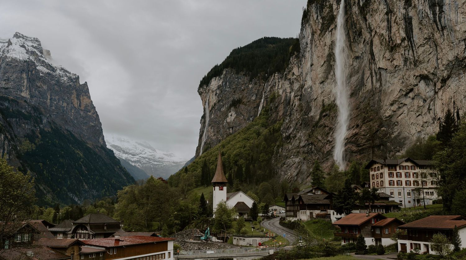 Dramatic mountain landscape with towering cliffs and small buildings nestled in Swiss valley.