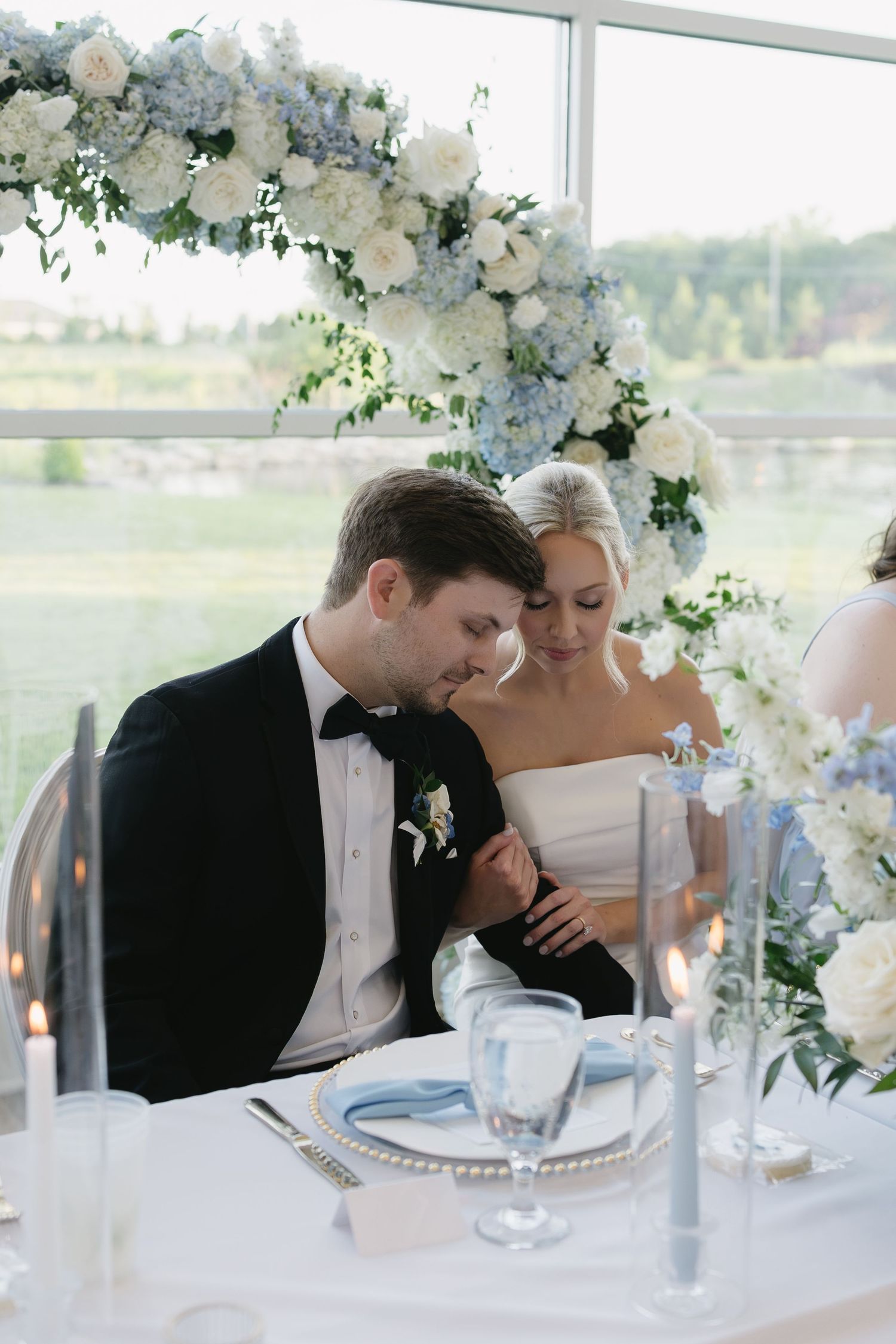 Bride and groom share an intimate moment at their elegant wedding reception table adorned with blue and white floral arrangements.