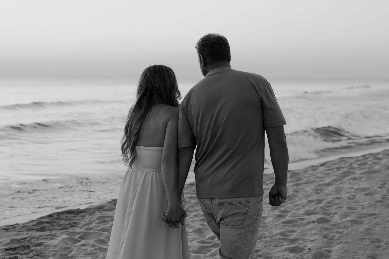 Silhouette of a couple walking along the shoreline during sunset with waves crashing nearby.