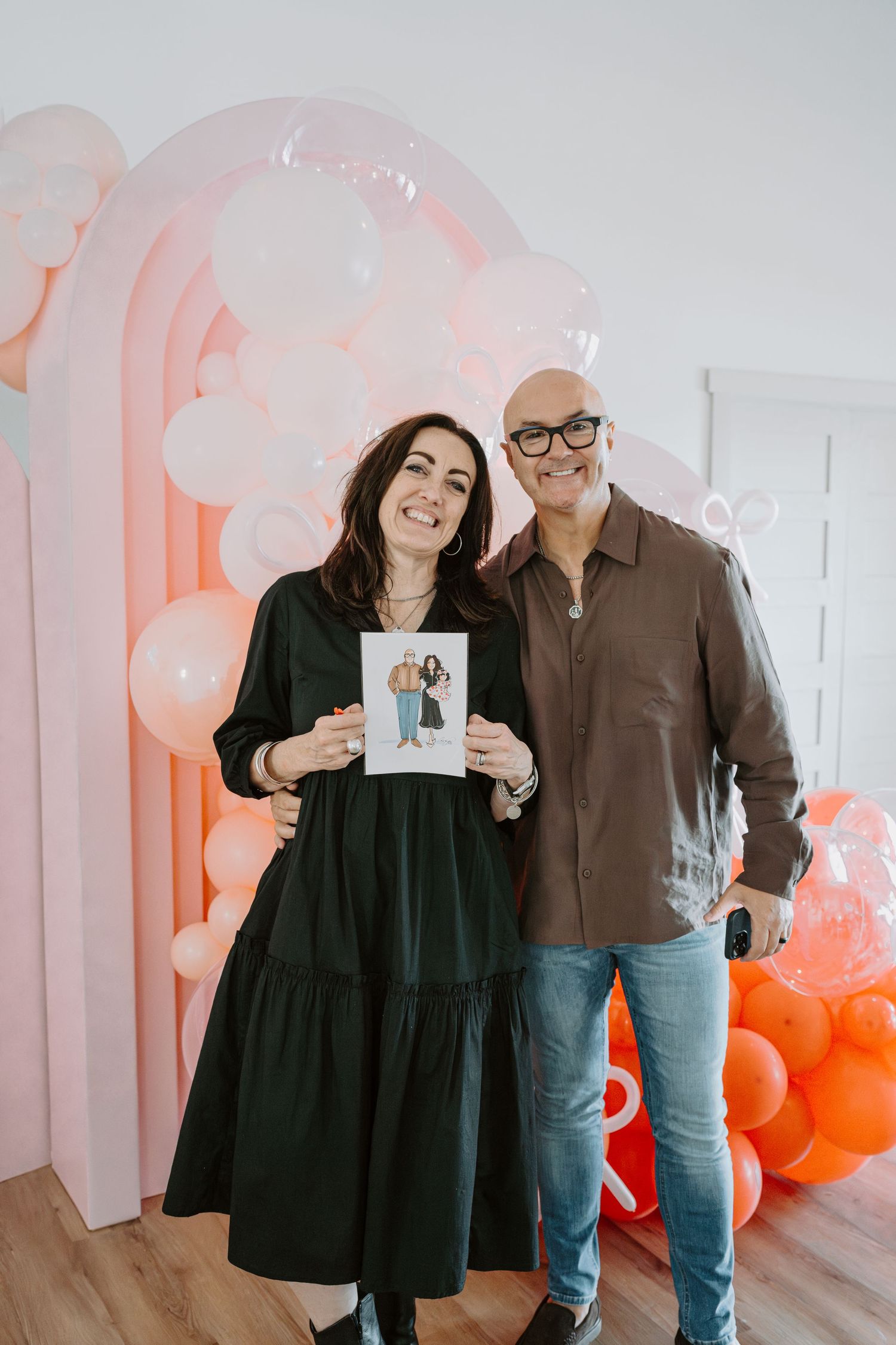 People showing photos in bright room decorated with pink and orange balloon arch.