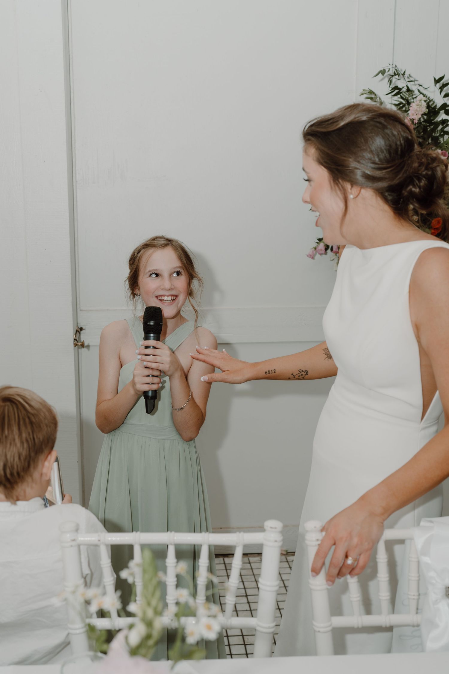 Wedding guests share playful moments at a white-themed reception with chiavari chairs.