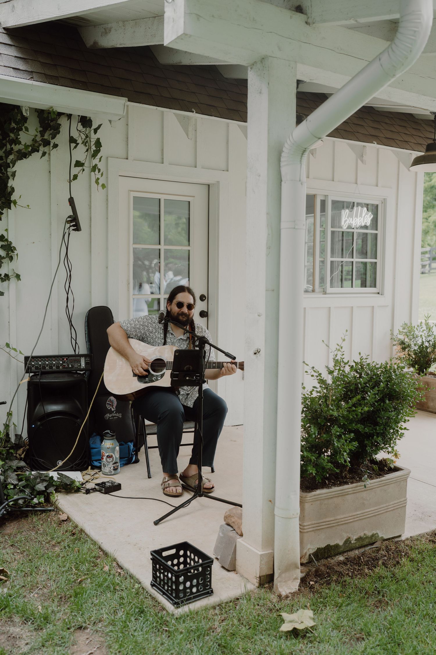 Musicians setting up equipment under a white covered porch area.