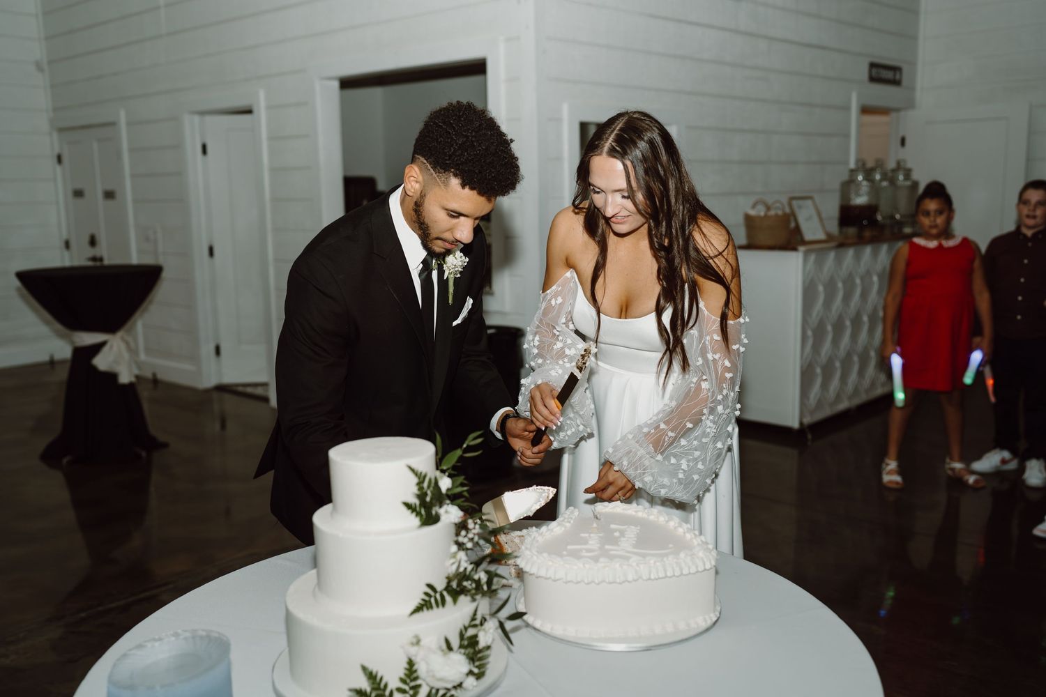 Couple cutting their elegant white wedding cake decorated with greenery.