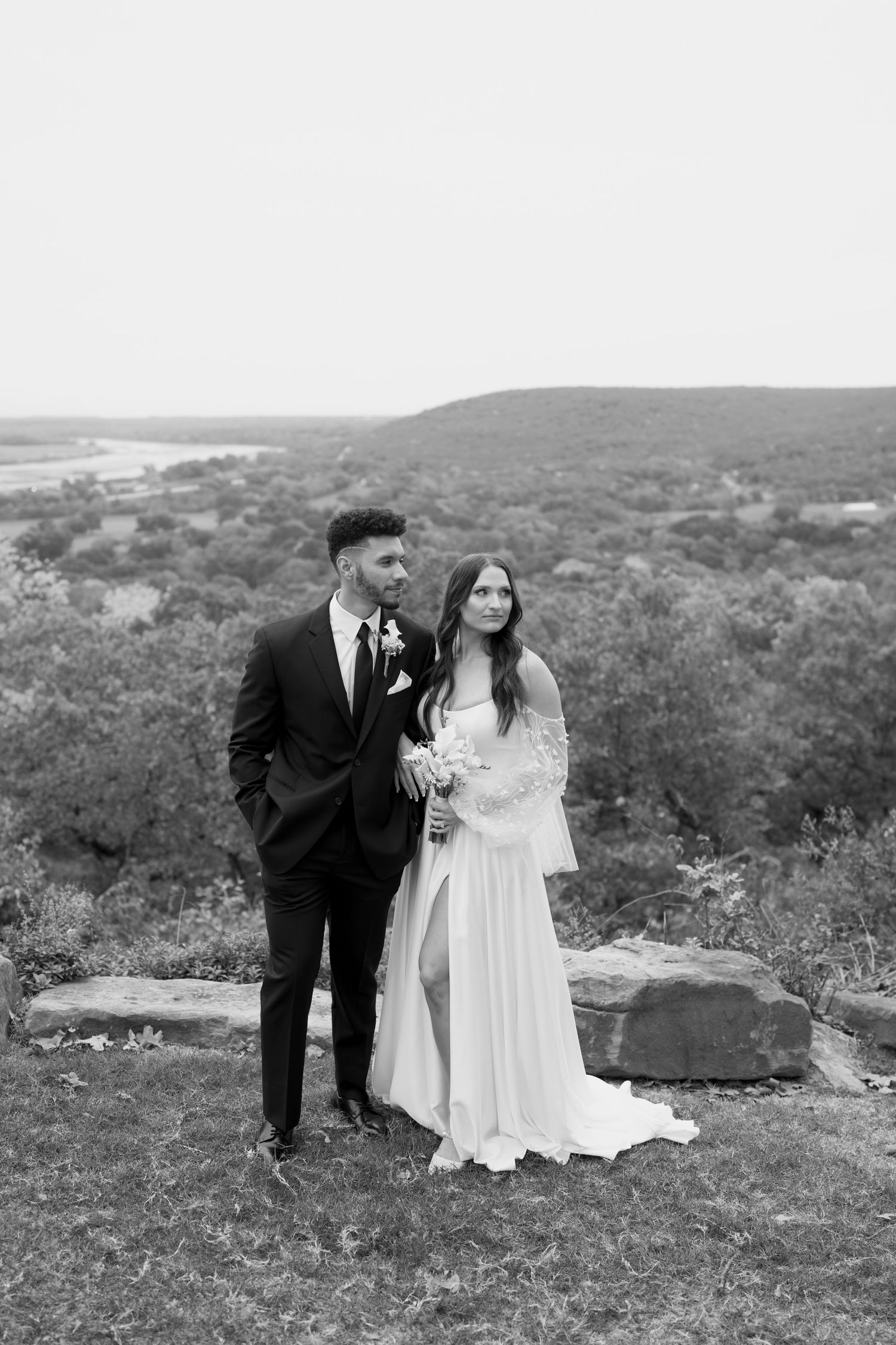Black and white portrait of couple embracing on scenic overlook during wedding.