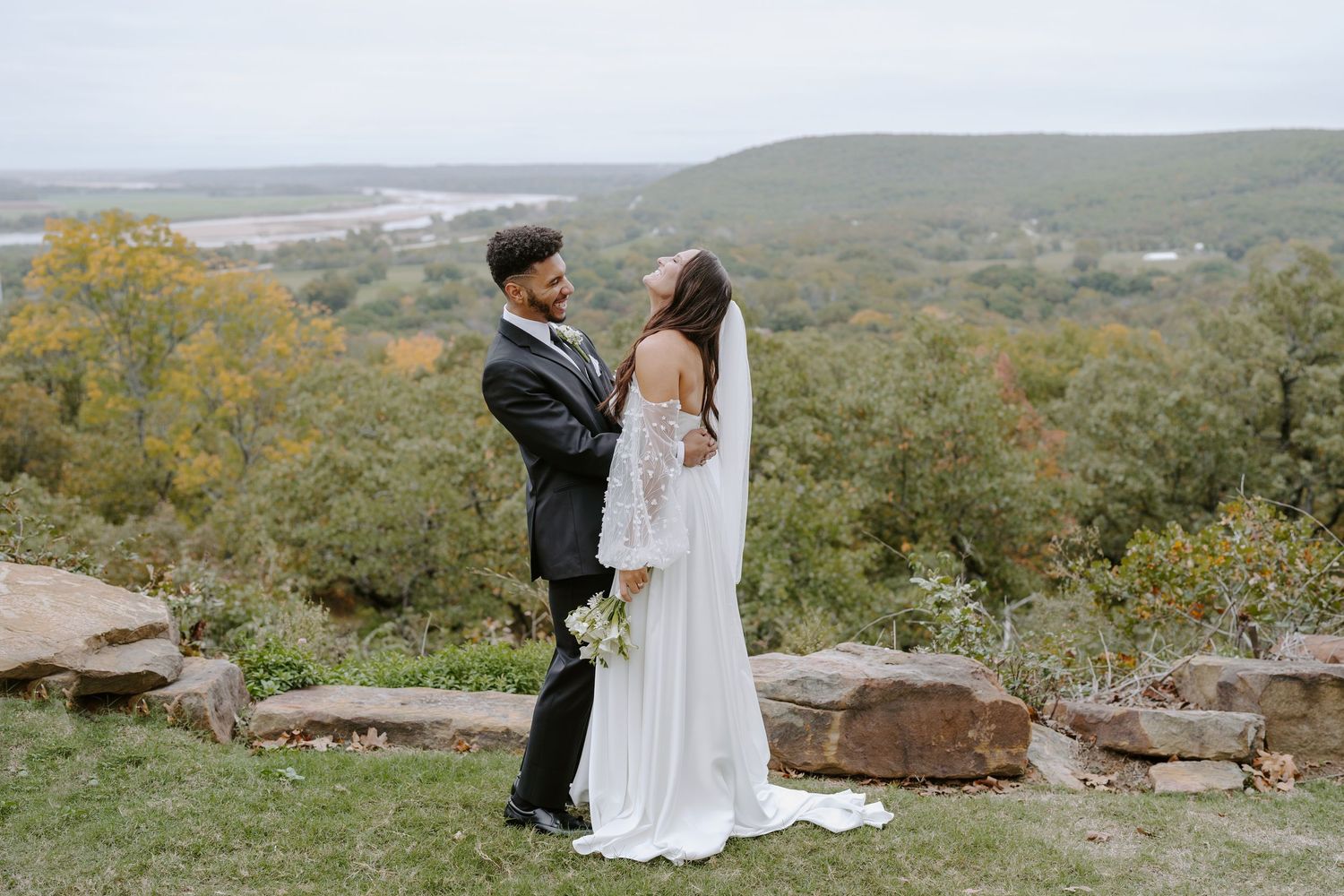 A wedding couple shares a romantic moment on a scenic overlook surrounded by autumn colors.