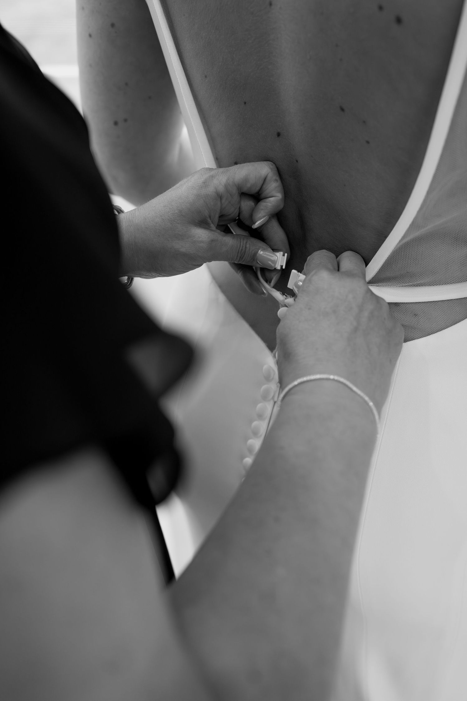 Black and white close-up of wedding dress being buttoned up.