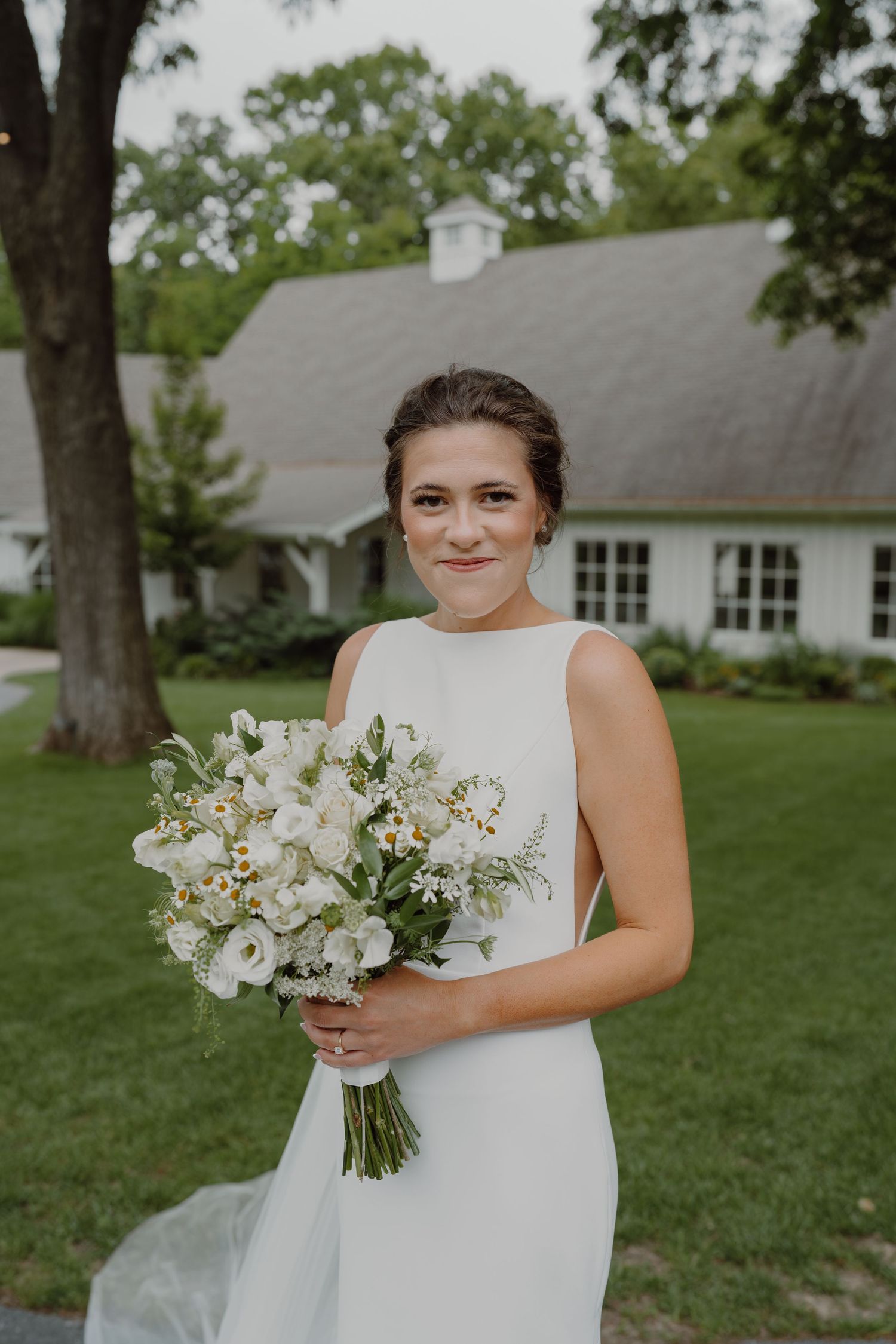 A bride holds a beautiful white floral bouquet while standing outdoors near a white building.