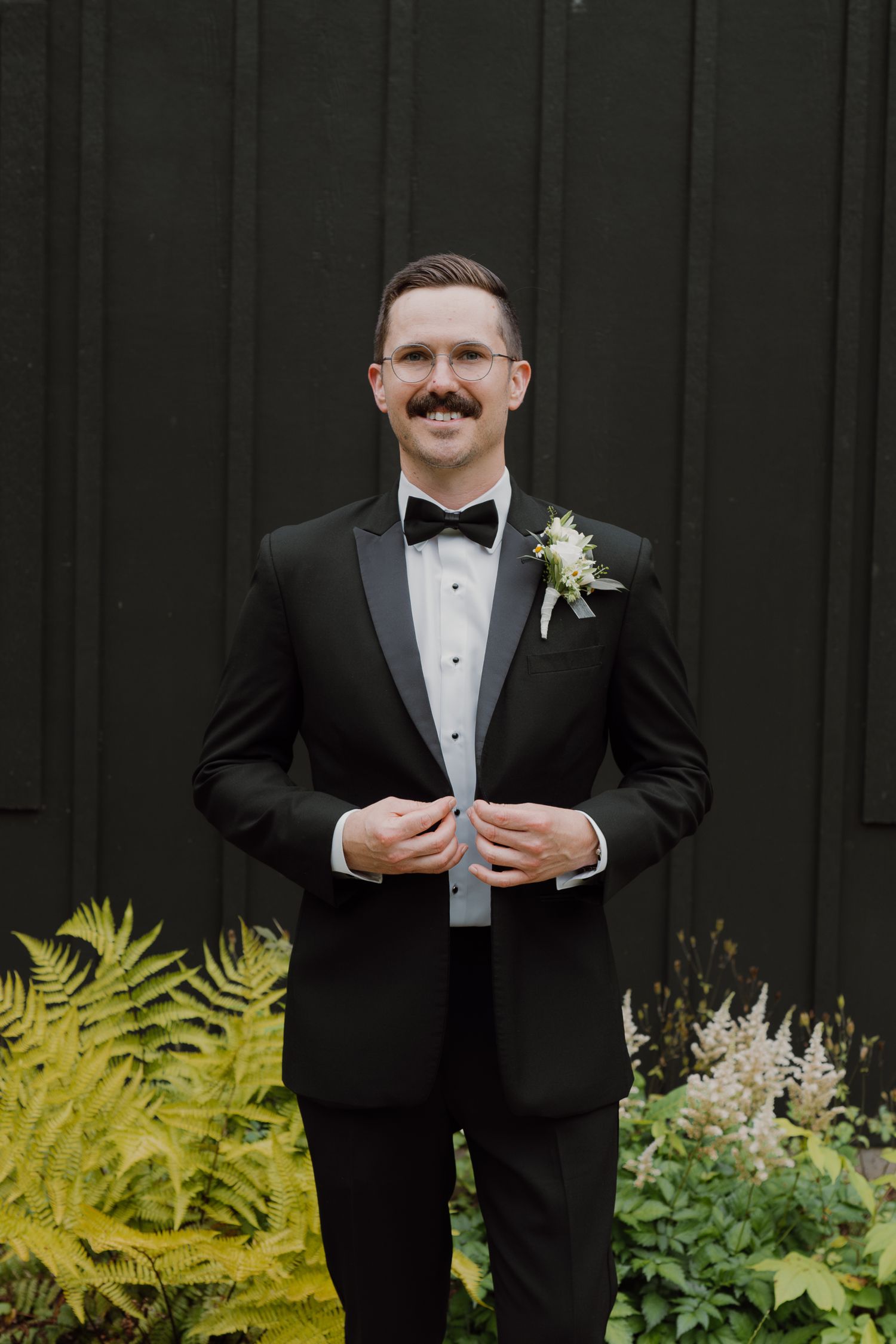 Formal portrait against dark wall with bright yellow ferns and garden plants.
