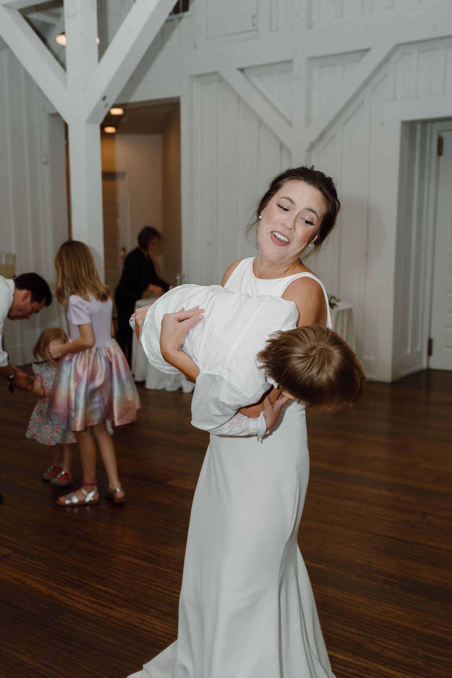 Dancing celebration in a bright white reception hall with hardwood floors.