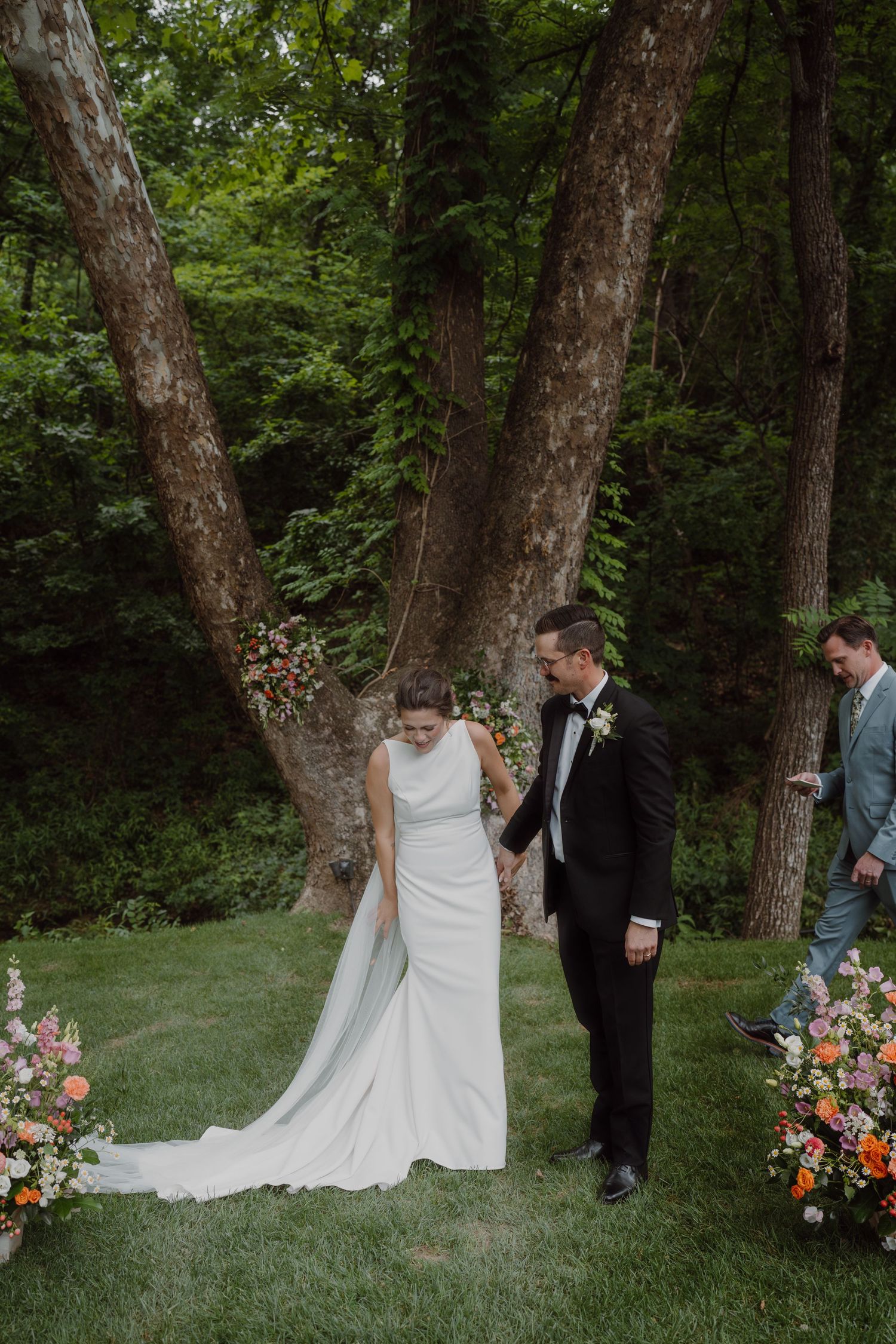 Wedding ceremony setup in a forest clearing with floral arrangements between tall trees.